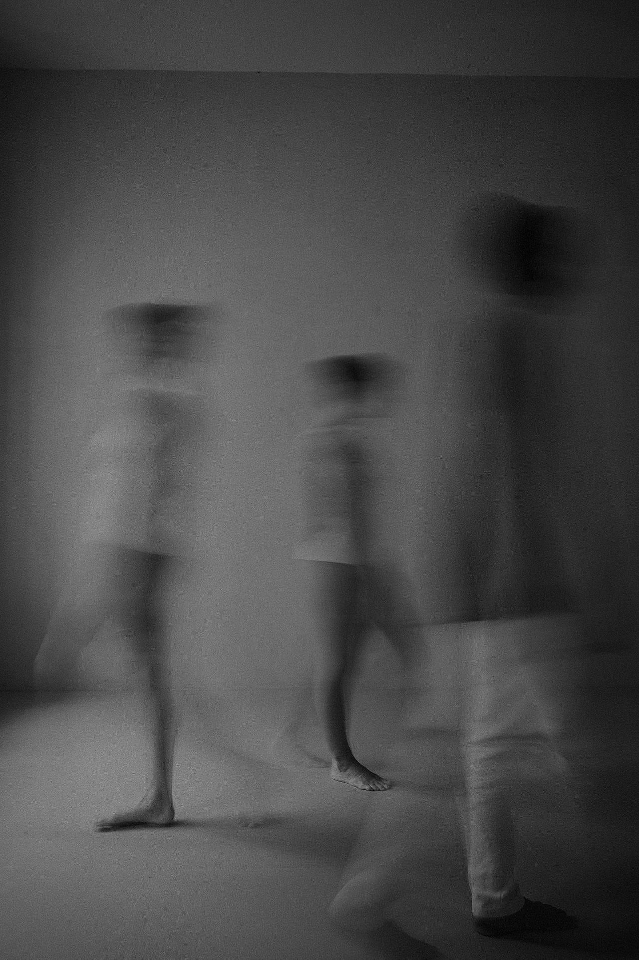 Blurry black and white photo of three people walking in a room, with motion blur creating a ghostly effect.