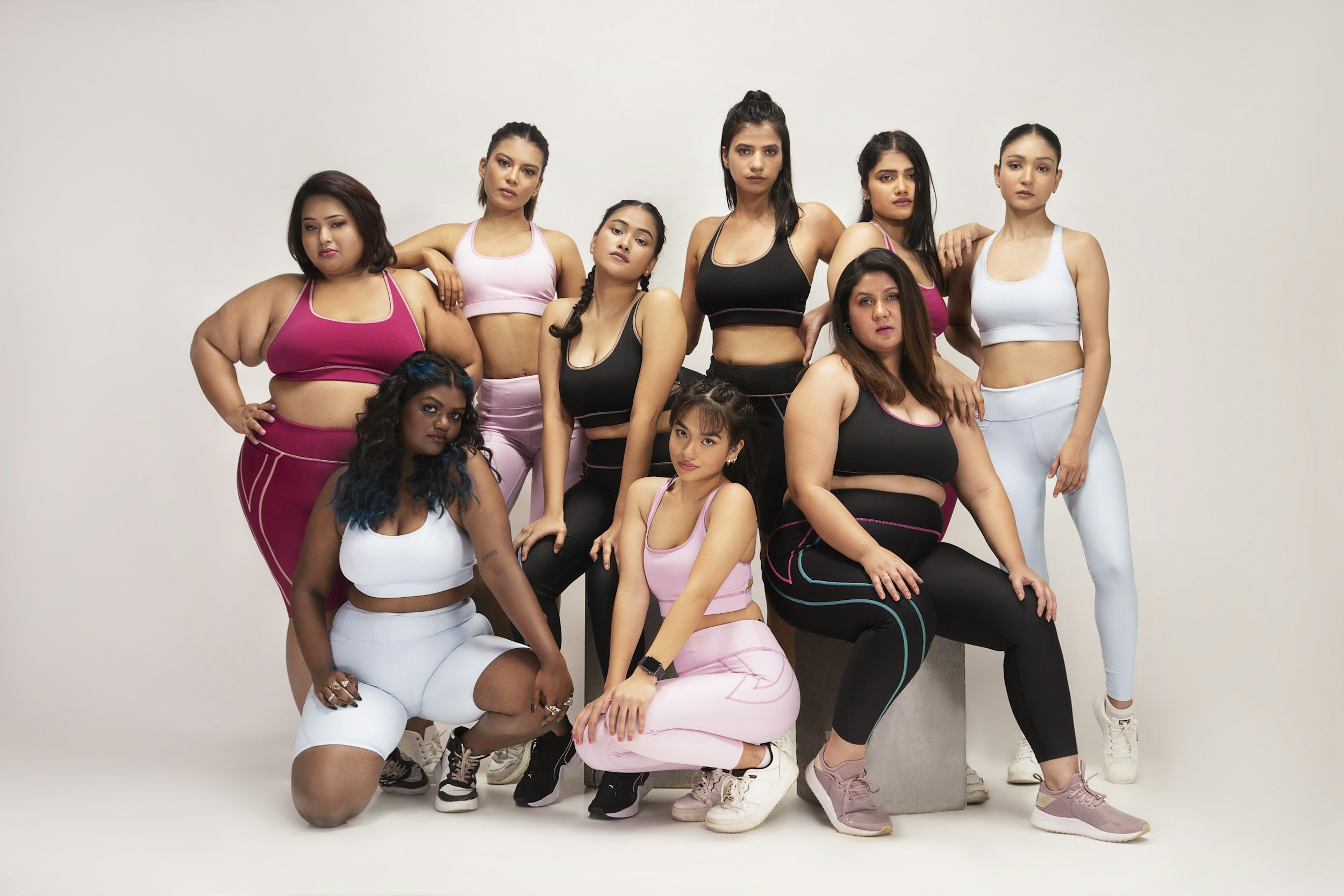 Eine Gruppe von Frauen verschiedener ethnischer Hintergründe in sportlicher Kleidung posiert vor einem weißen Hintergrund.
