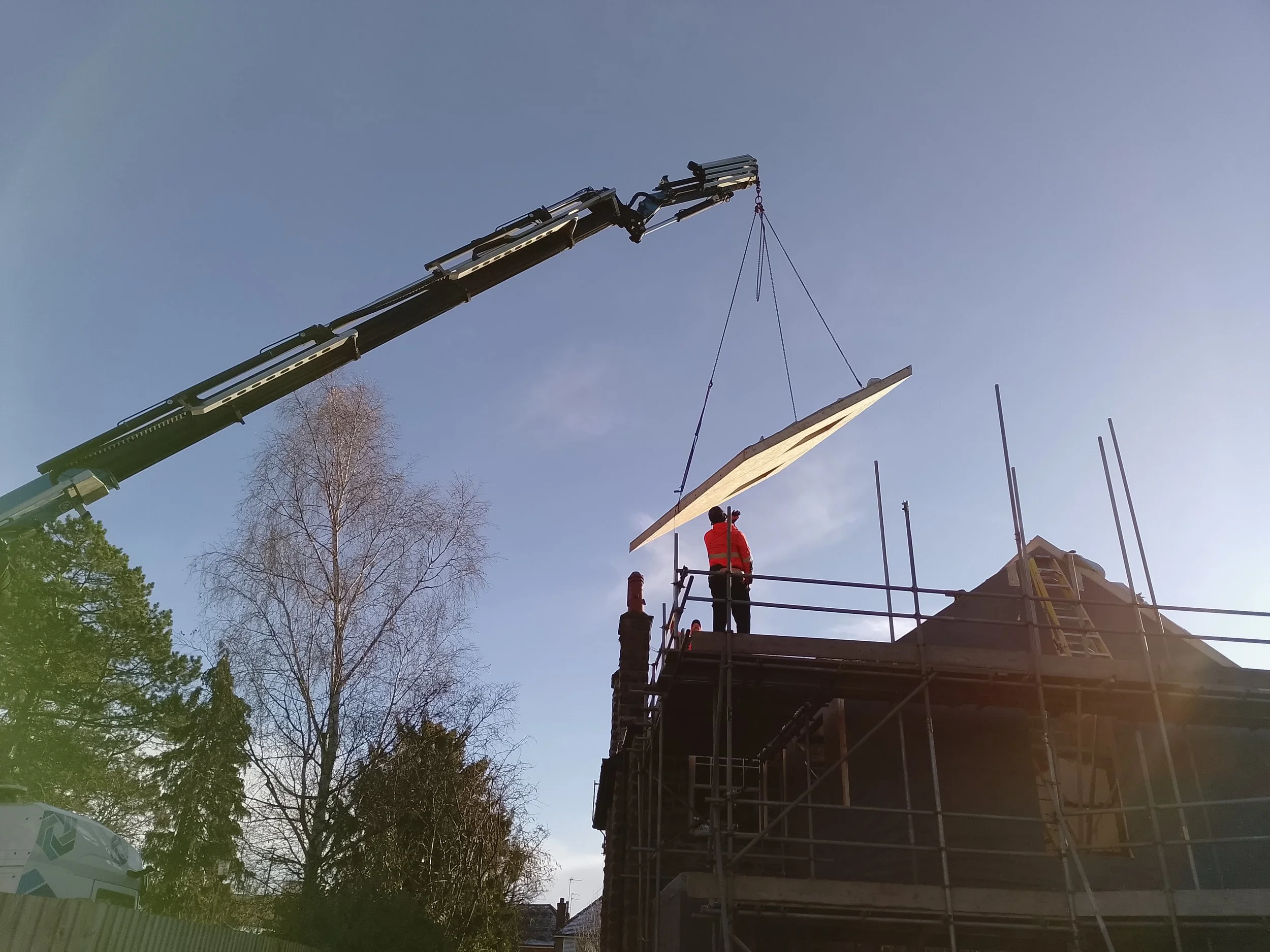 Crane lifting SIPs panel into place for roof construction at SIPs building project in Harrogate