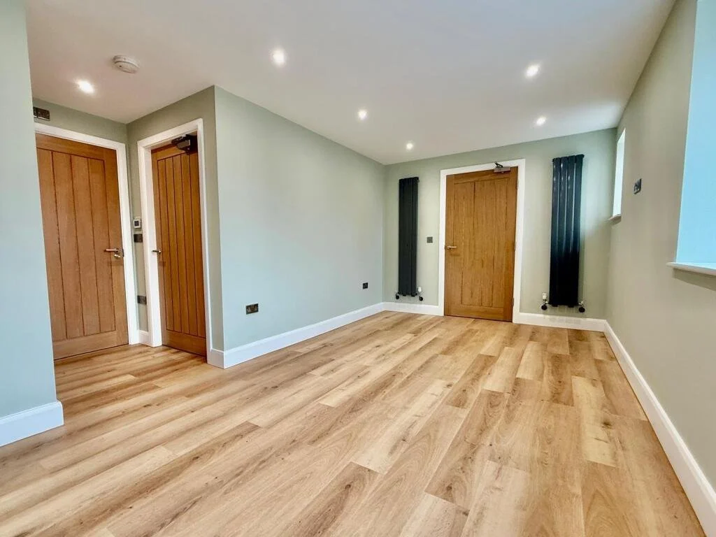 Living room with oak doors, light-colored walls, LVT flooring, and custom colour column radiators flanking the entrance.