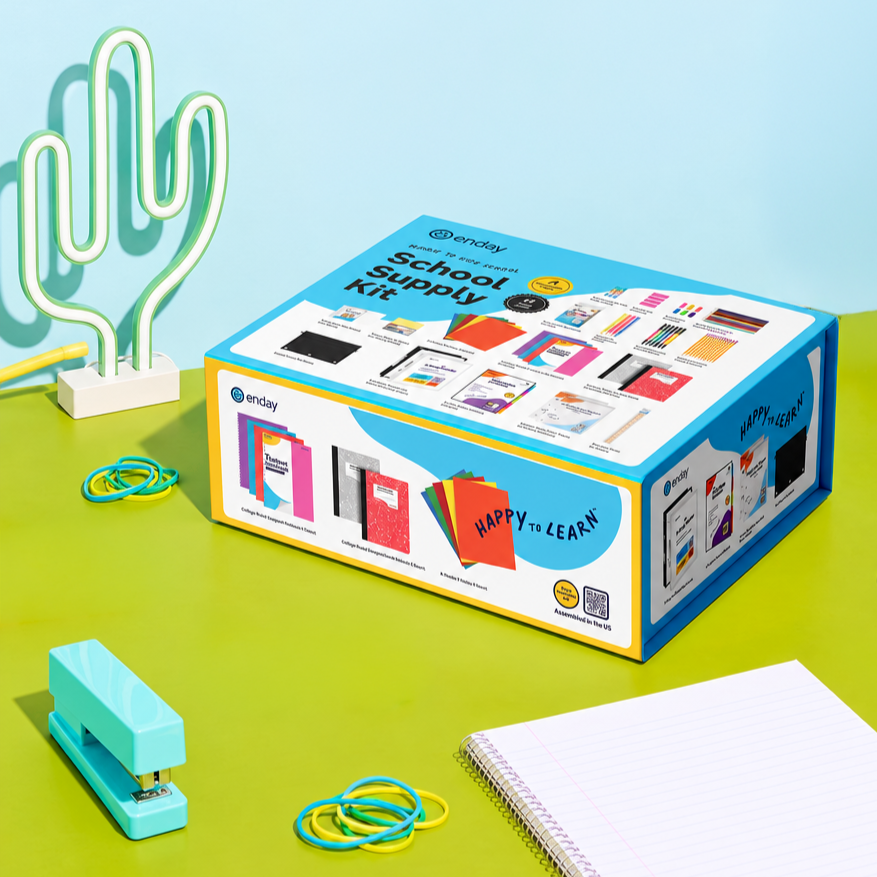 School supply kit box with various educational materials, rubber bands, a stapler, and a notebook on a green table, with a neon cactus lamp in the background.