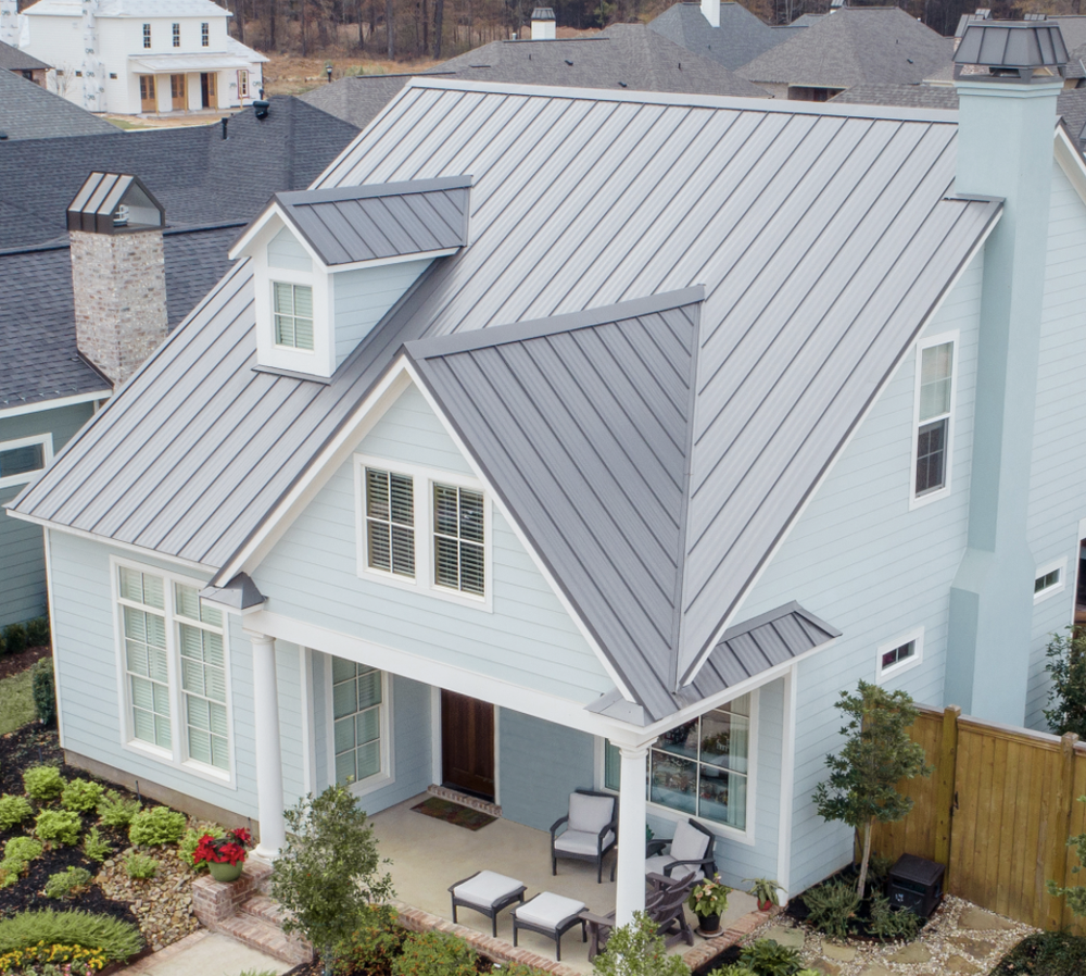 A new, light gray McElroy metal roofing system on a light blue house with plants in front..