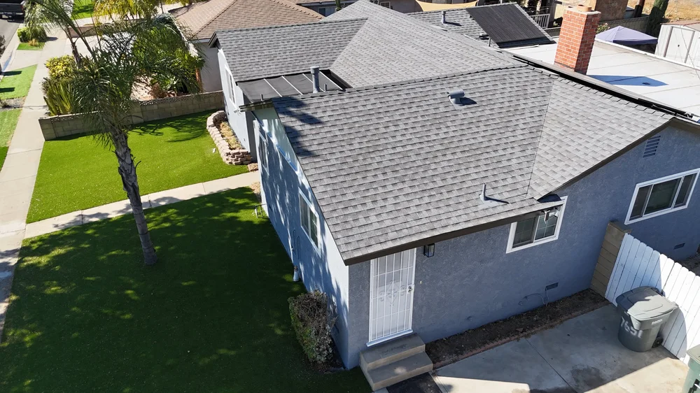 Residential roof on a light blue-gray home in Buena Park with palm tree in front yard.