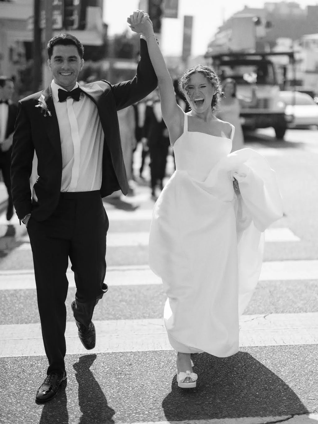Happy couple walking across Sunset Boulevard in West Hollywood with their hands in the air cheering for their new marriage.