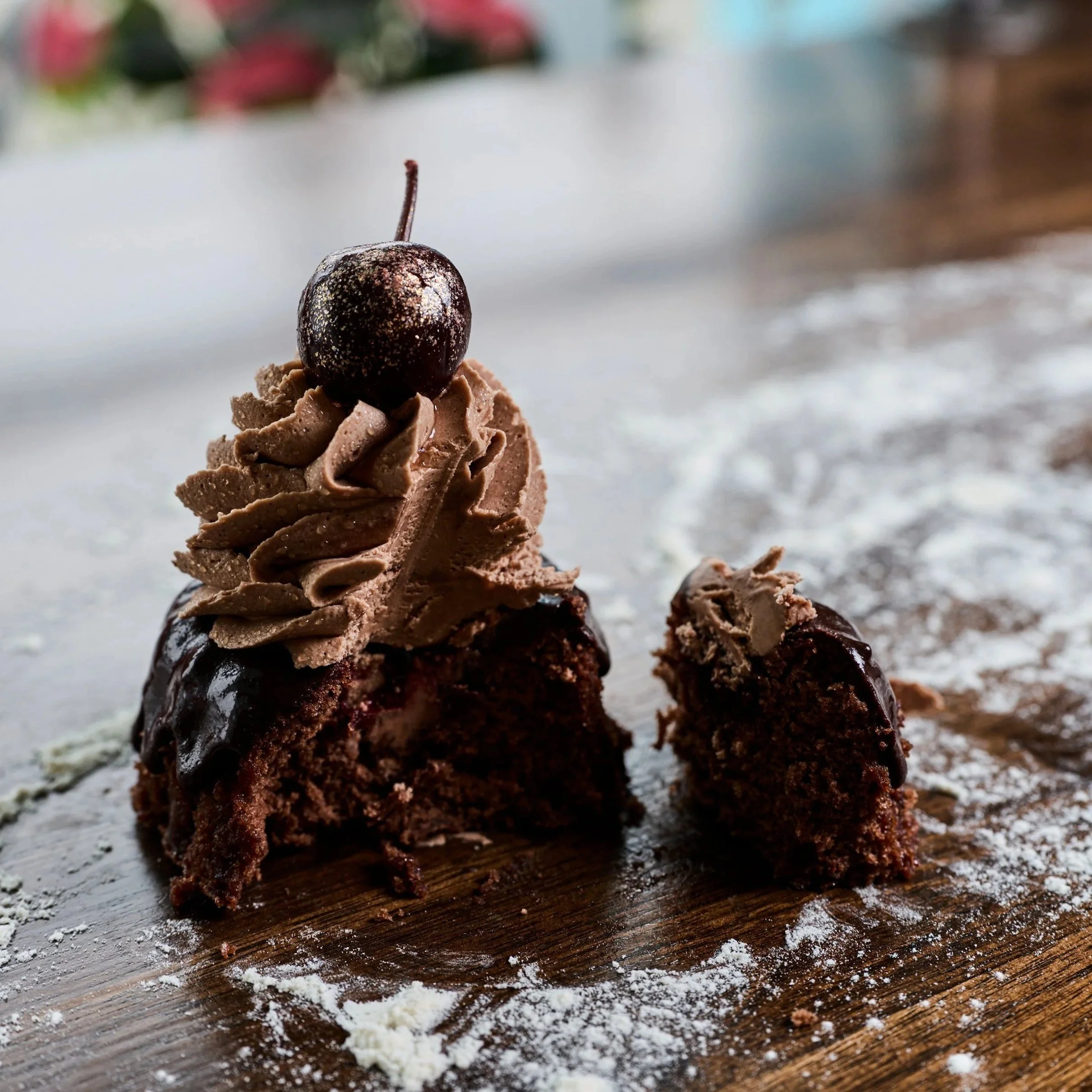 A chocolate cake with chocolate frosting topped with a whipped chocolate swirl and a cherry.