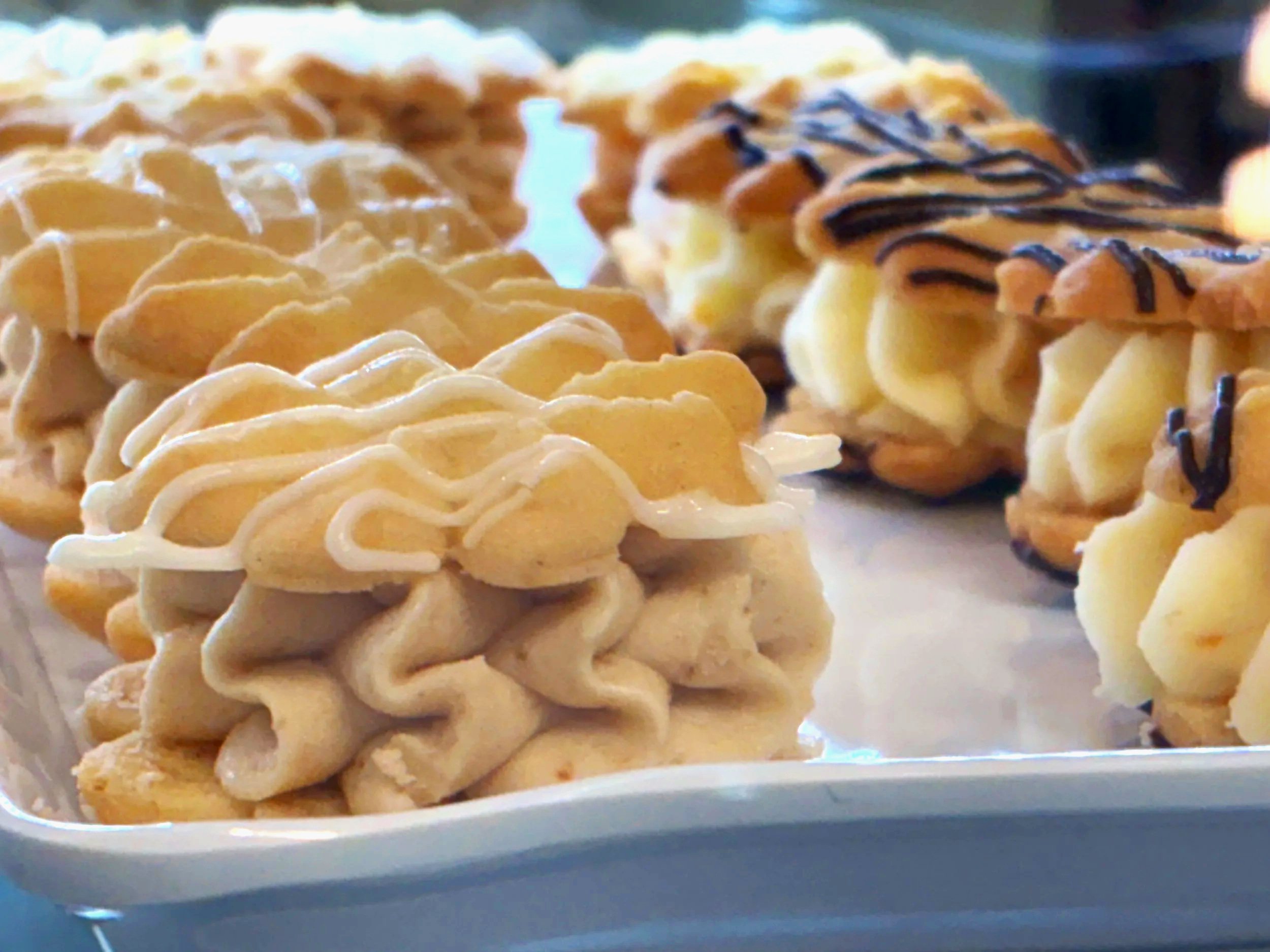 Close-up of decorated butter cookies on a white tray, with frosting and chocolate drizzle on some.
