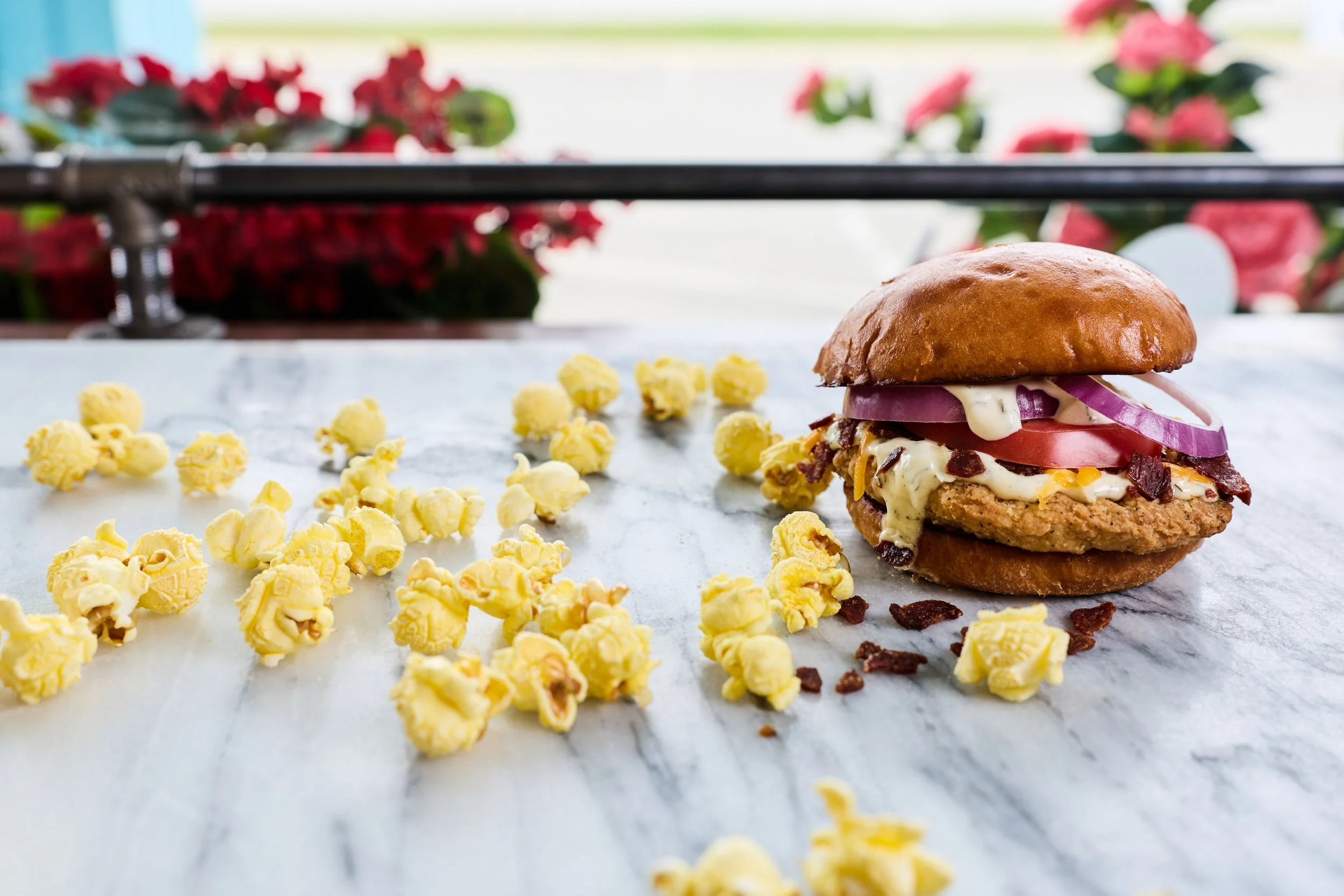 Breaded chicken with tomato, onions, bacon, and ranch on a toasted brioche bun with popcorn.