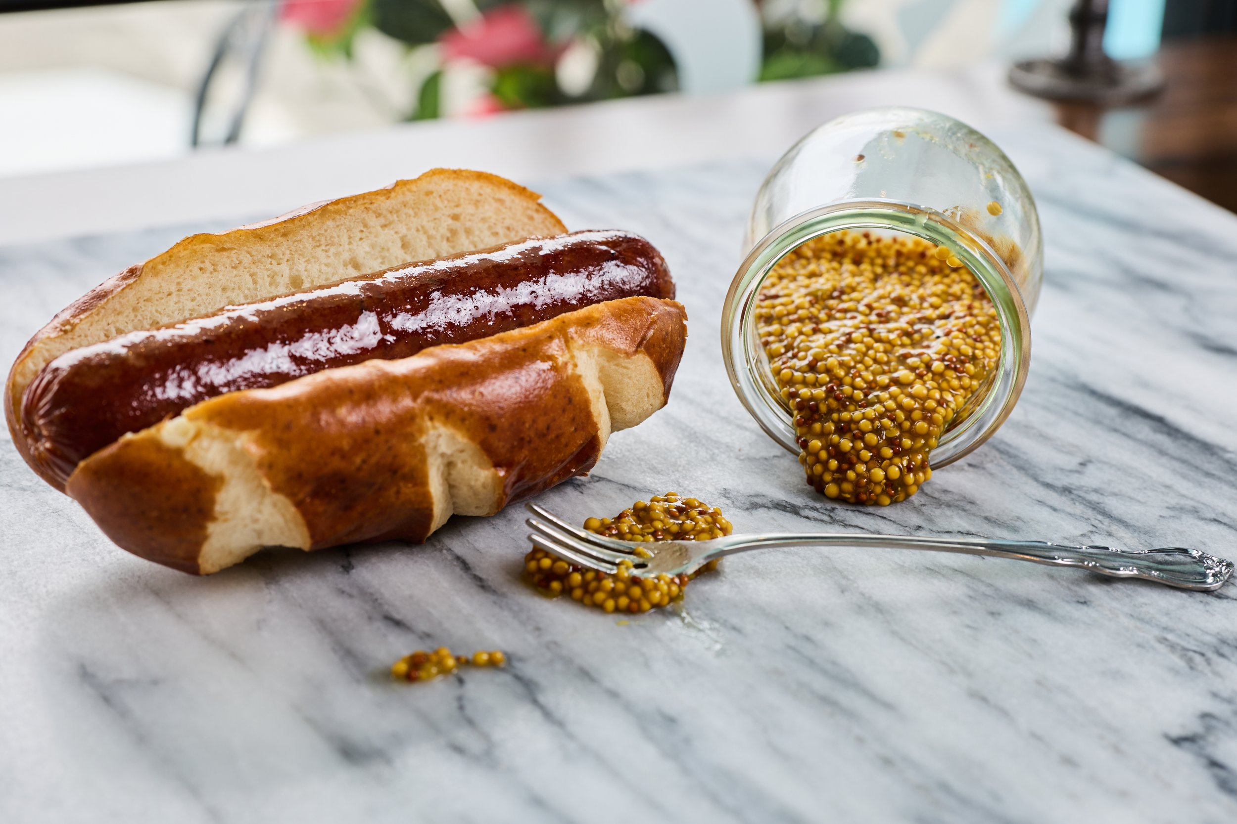 Brisket bratwurst in a pretzel bun with a jar of IPA mustard.