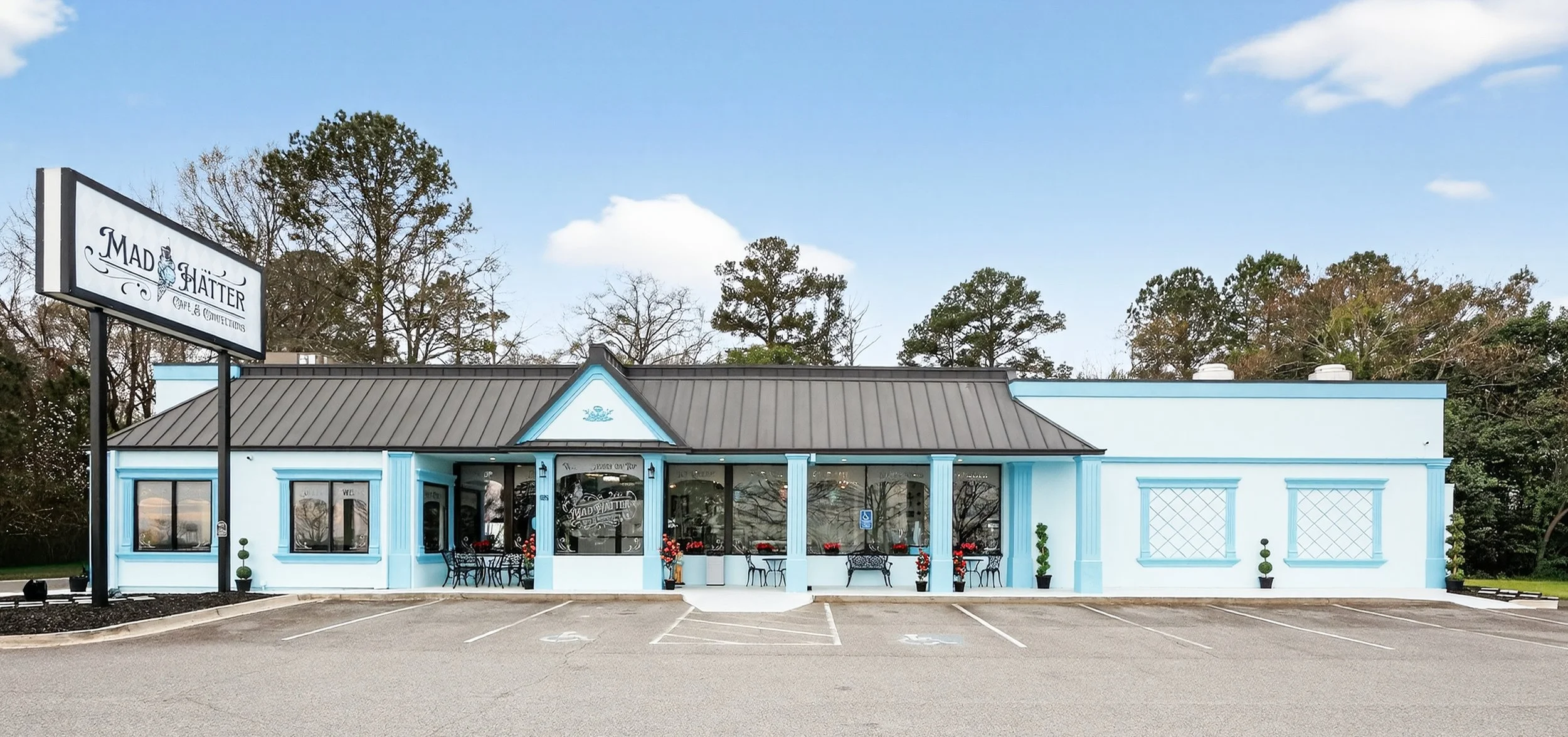 Exterior of a light blue restaurant with large front windows, outdoor seating, and a sign that reads 'Mad Hatter Café & Confections.'
