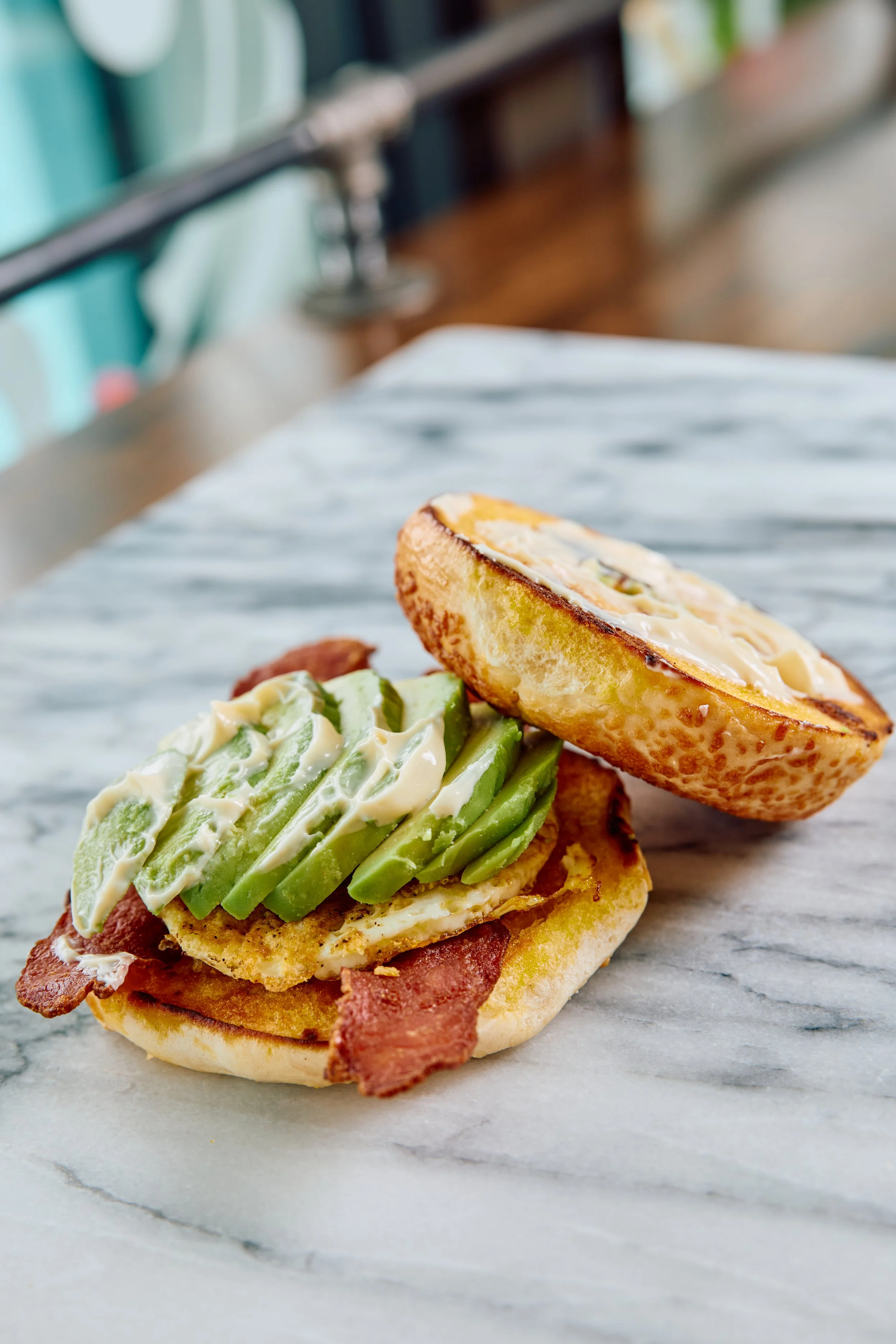 Close-up of an avocado, egg and bacon breakfast sandwich on a toasted bagel.