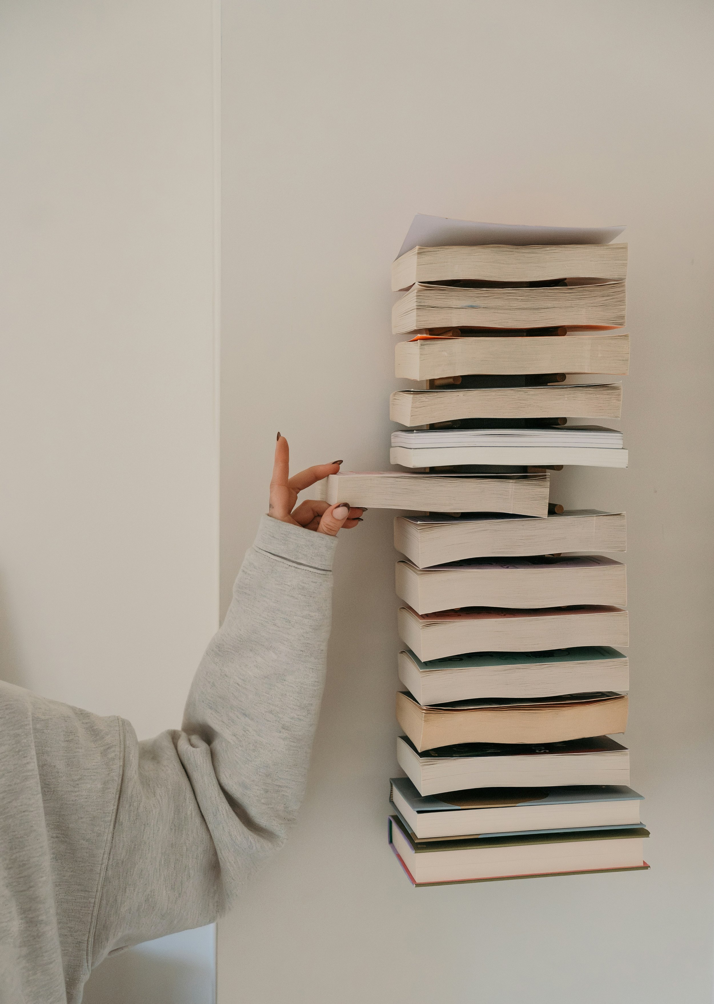 girl in gray sweatshirt gently tapping stack of old books on warm cream background