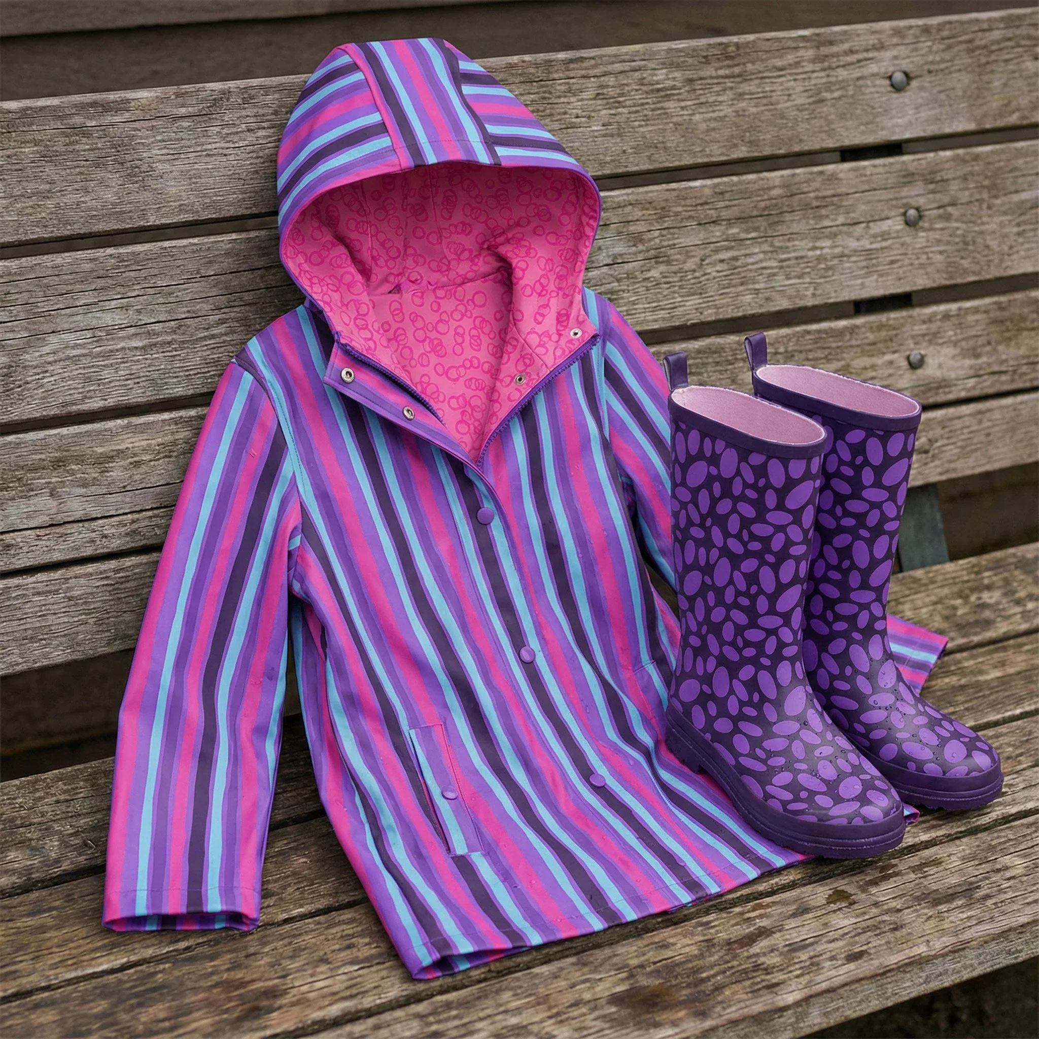 Colorful striped raincoat paired with coordinating purple rain boots featuring a playful abstract dot pattern. This vibrant kids rainwear design showcases bold stripes, whimsical textures, and a modern color palette, making it ideal for children’s ap