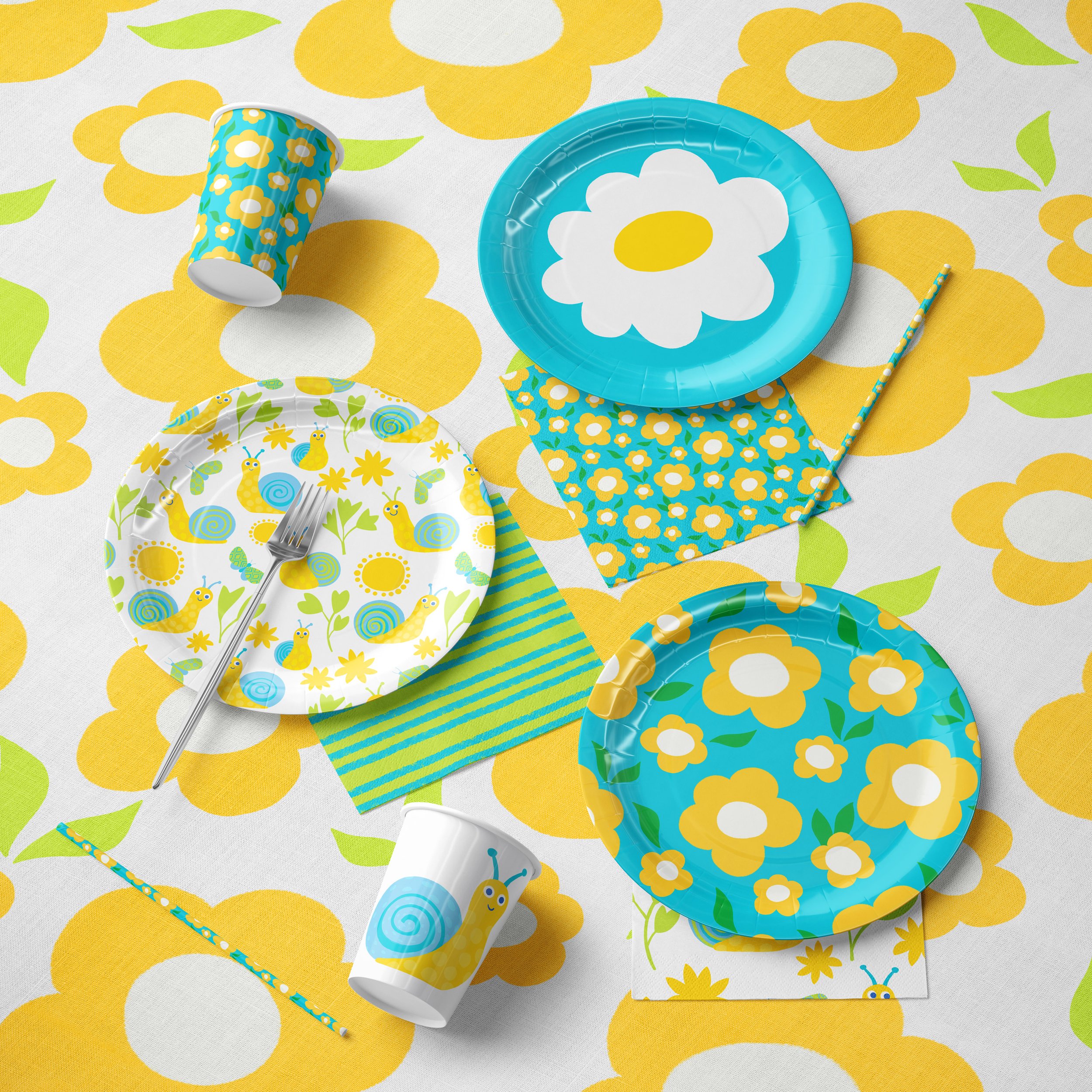 Party table setting with blue and yellow floral-themed paper plates, cups, napkins, and straws on a matching tablecloth.