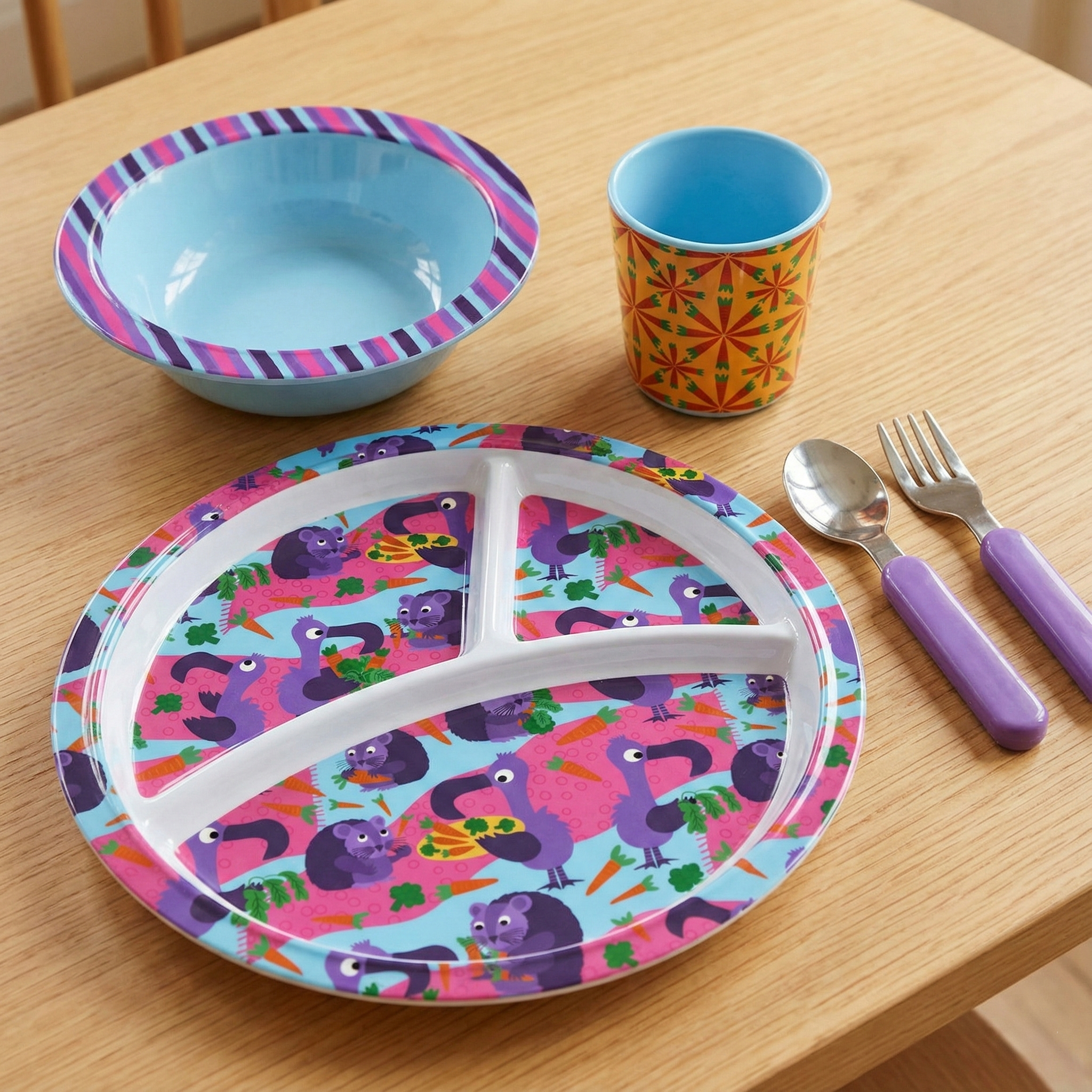 Colorful children’s dinnerware set featuring a playful divided melamine plate, matching bowl, cup, and utensils from the Eat Your Veggies collection. Whimsical animal illustrations, carrots, broccoli, and garden motifs encourage joyful, stress-free m
