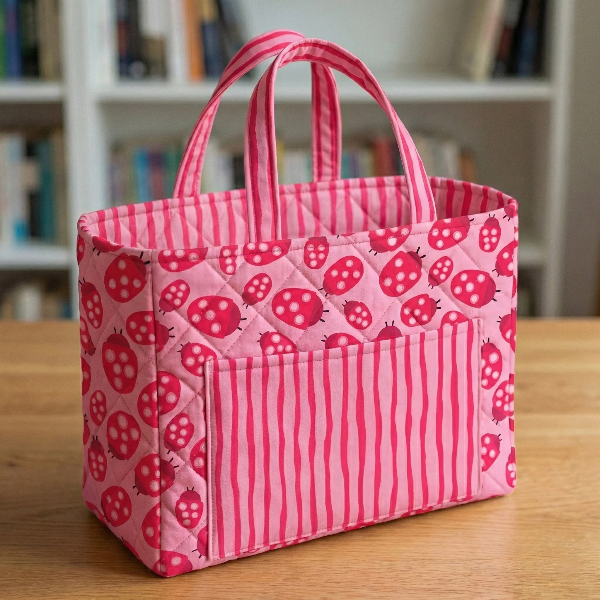 Pink quilted tote bag with playful red ladybug pattern and striped front pocket, handmade fabric accessory