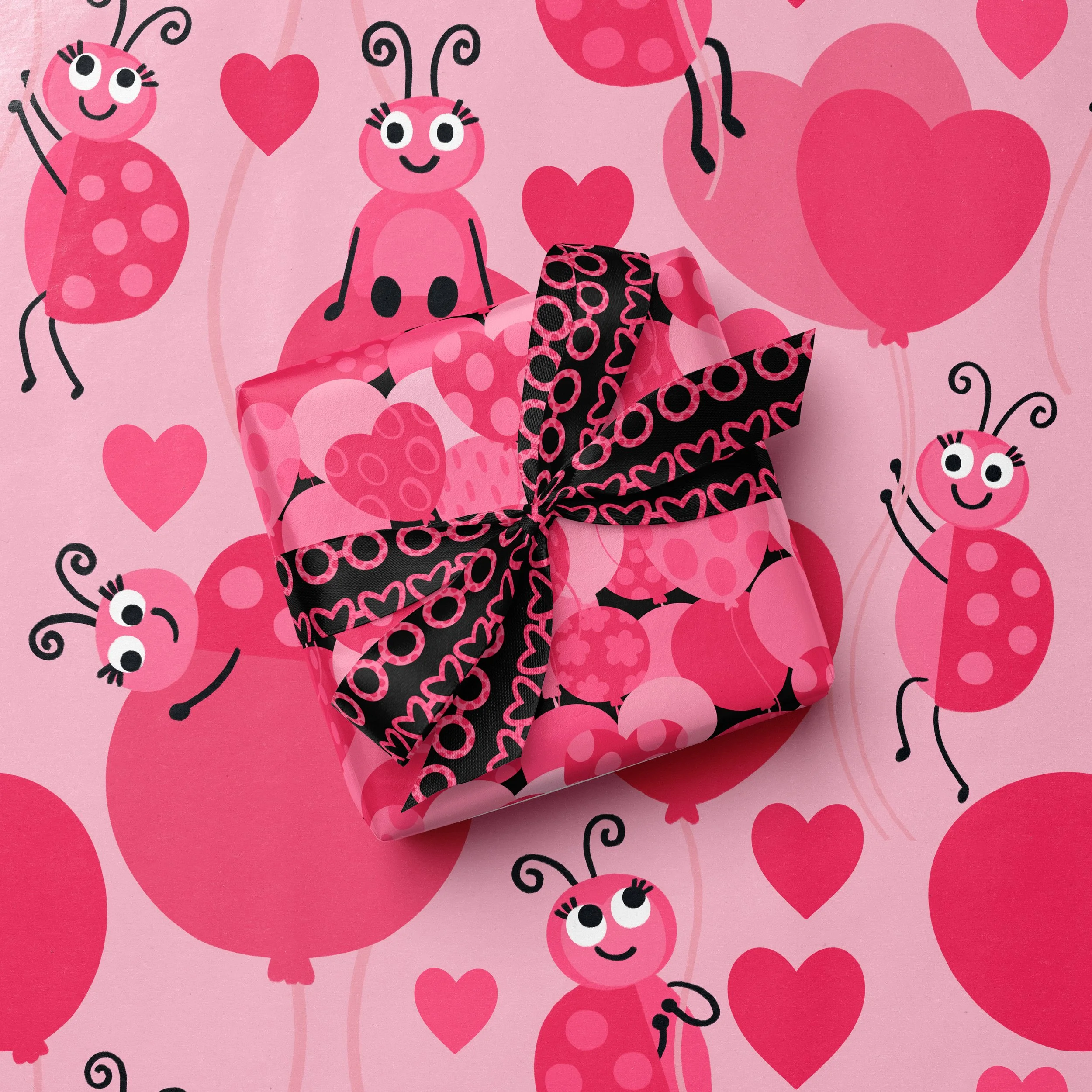 A pink gift box with a black ribbon, decorated with pink hearts and ladybugs, placed on a pink background with ladybug, balloon and heart illustrations.