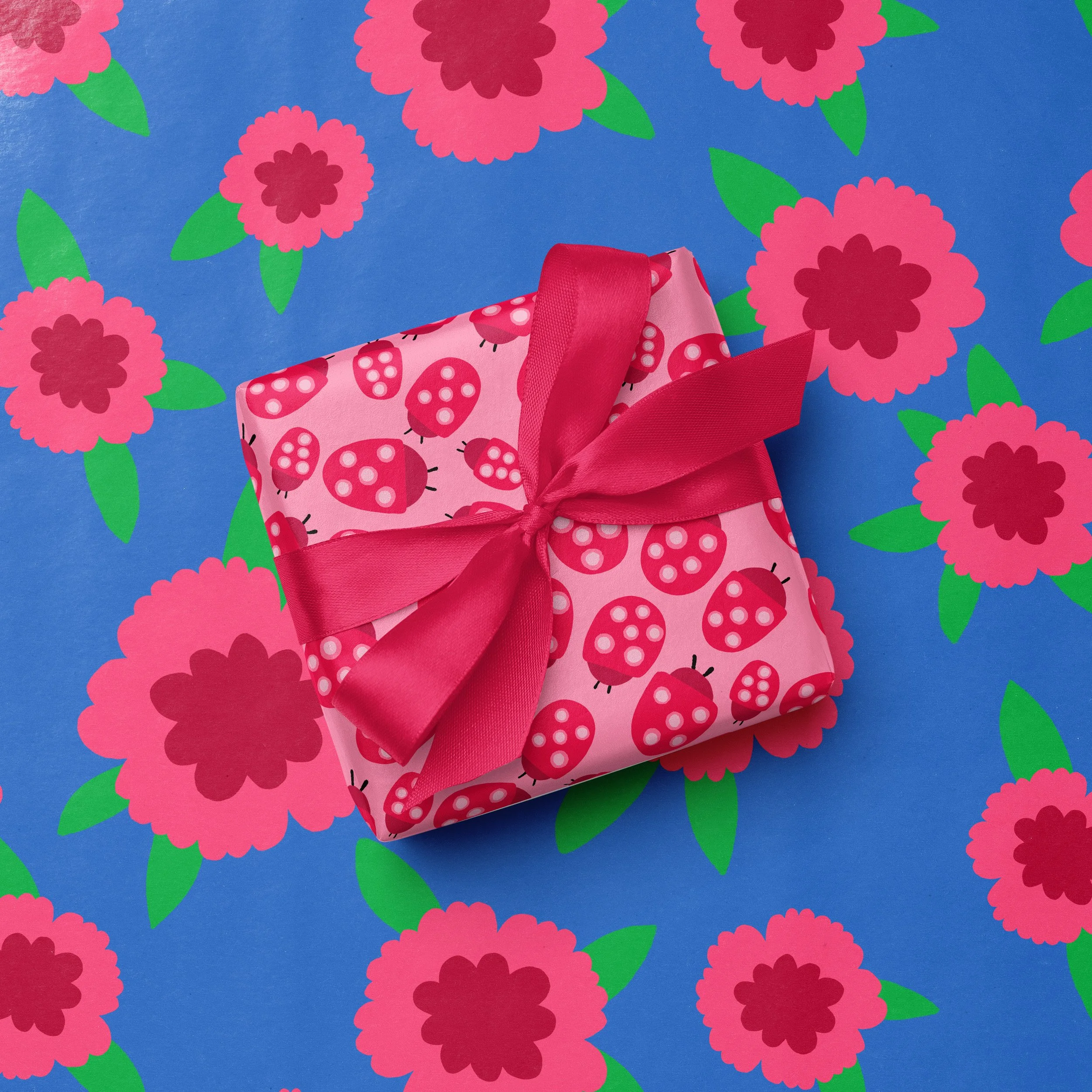 A pink gift box with ladybug pattern and a pink ribbon bow is on a blue background with pink and green floral design.