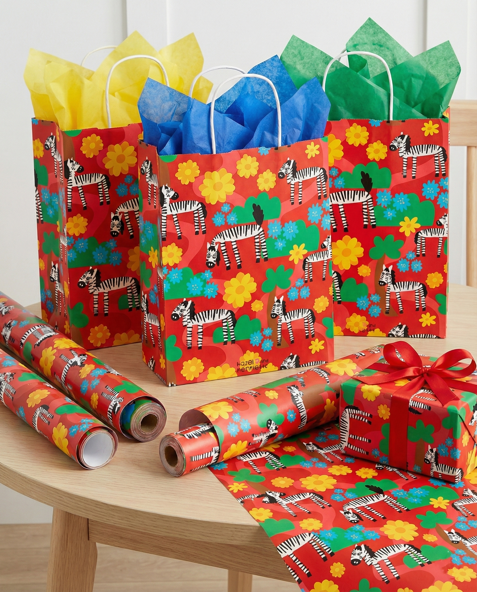 zebras in bloom illustration captured as gift bags and wrapping paper. illustration is on bright bold red background with black and white zebras  surrounded by trees, flowers and winding roads