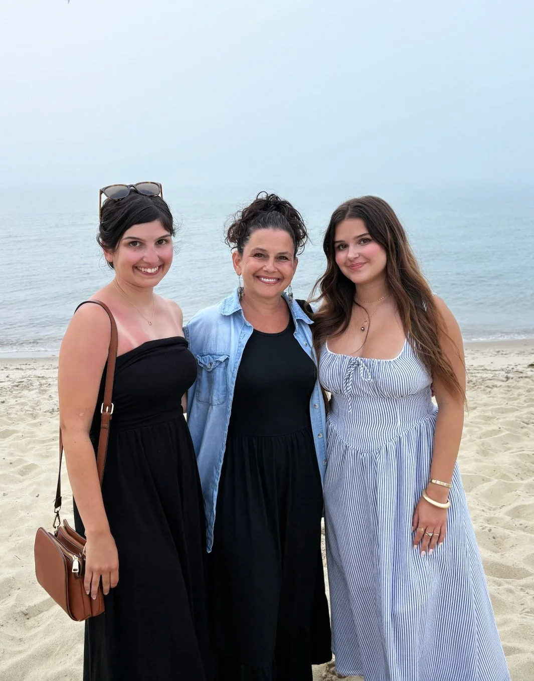 Three women standing on a beach with the ocean in the background, smiling at the camera.