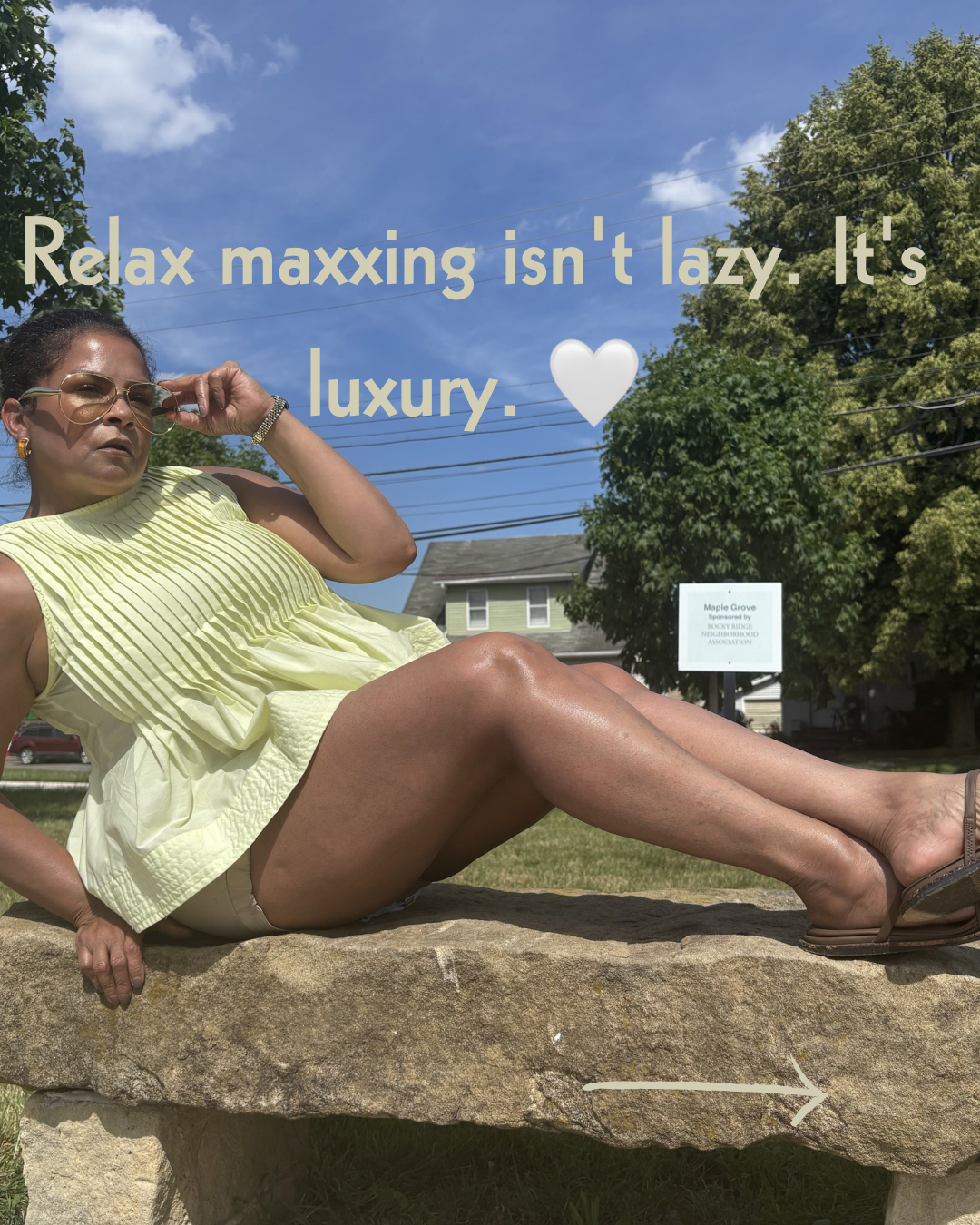 Keenya Willis lounging on a stone seat in a yellow top and sandals with text overlay reading Relax Maxxing isn’t lazy it’s luxury representing intentional rest as a lifestyle practice