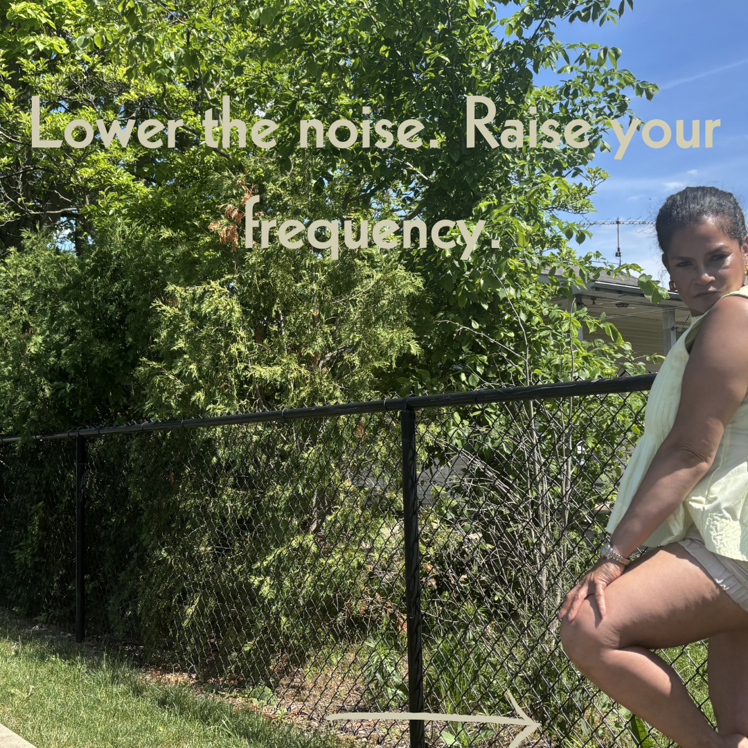 Keenya Willis looking over her shoulder at black fence in a yellow top and tan shorts with text overlay reading Lower the noise raise your frequency representing intentional environment curation for elevated living
