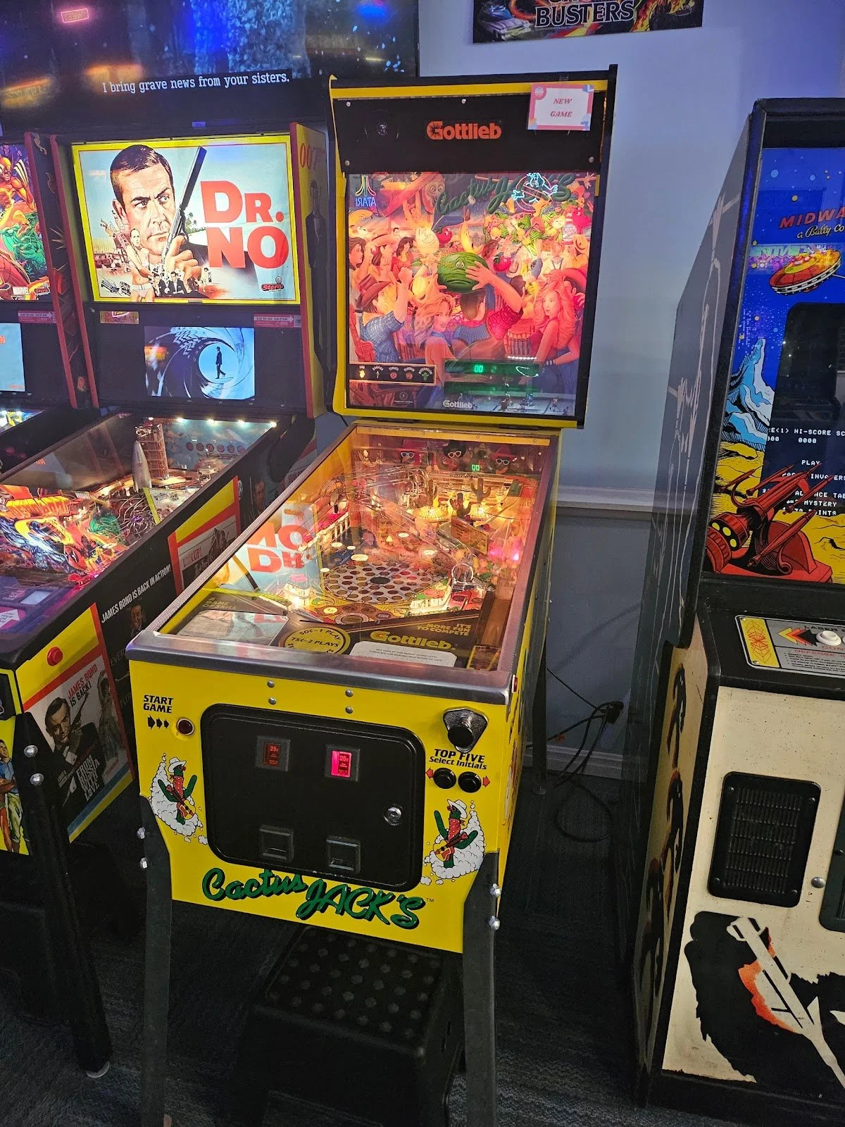 Cactus Jack's pinball machine with yellow cabinet, featuring cartoonish cactus characters and a tropical theme, surrounded by colorful arcade games.