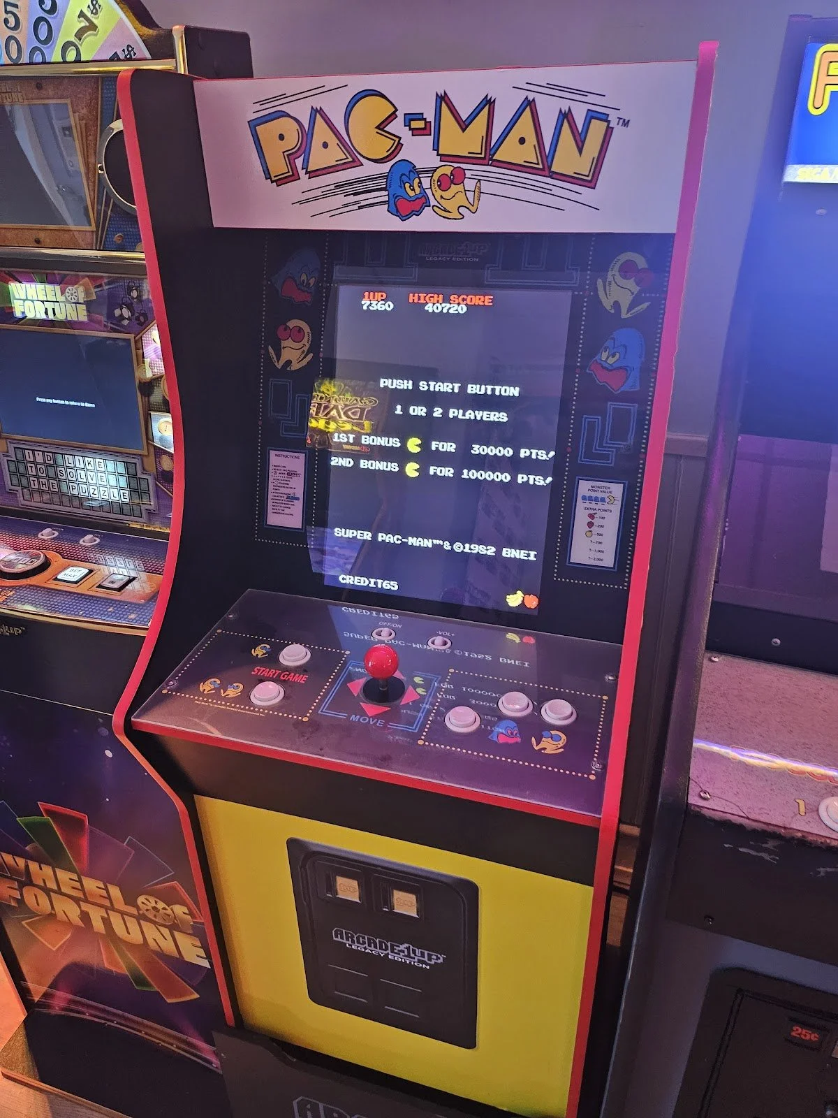 Pac-Man arcade game with colorful marquee and control panel, featuring a red joystick and buttons, in an arcade setting.