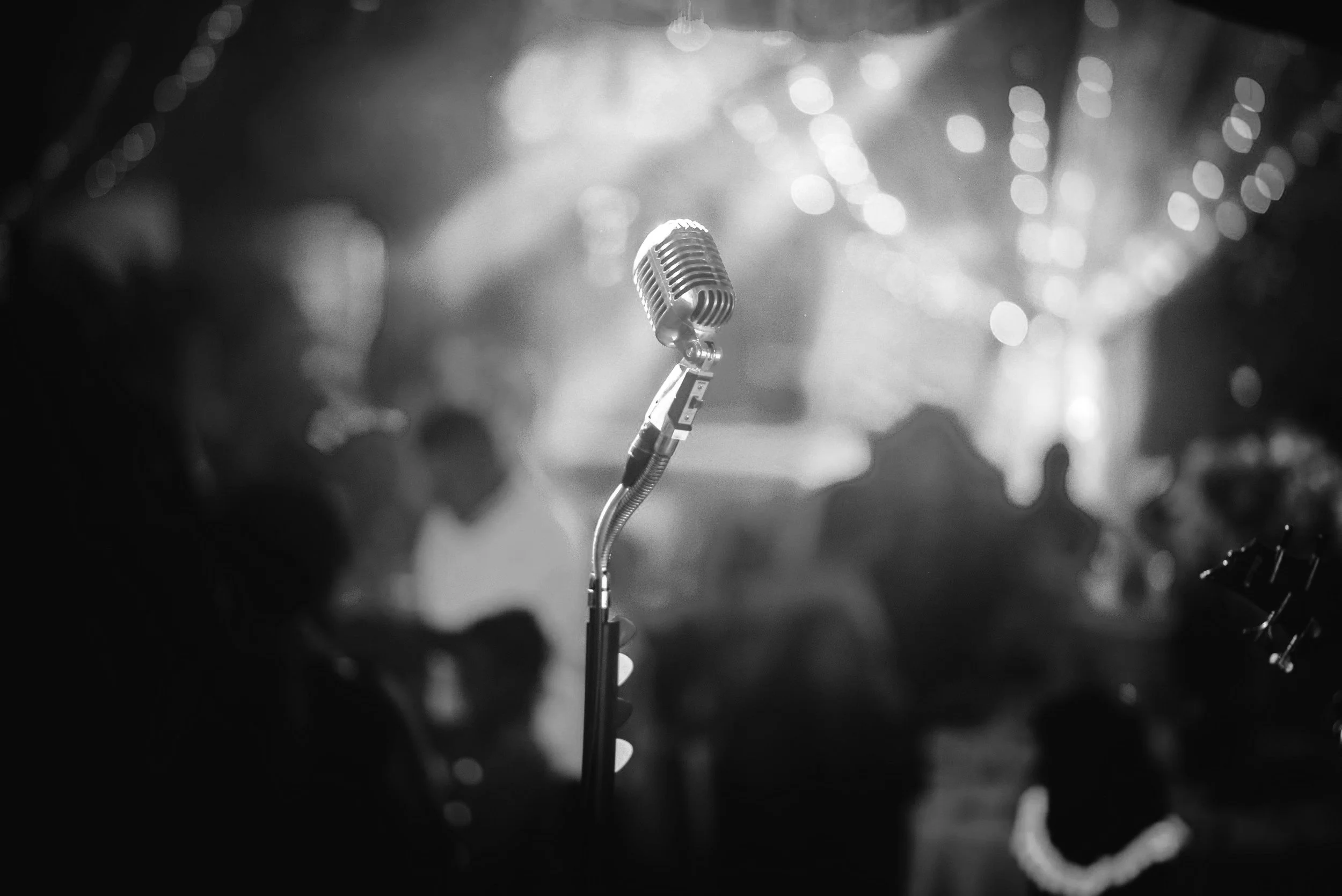 A vintage microphone on a stand in a dimly lit, blurred setting with people in the background, at a well known live performance event.