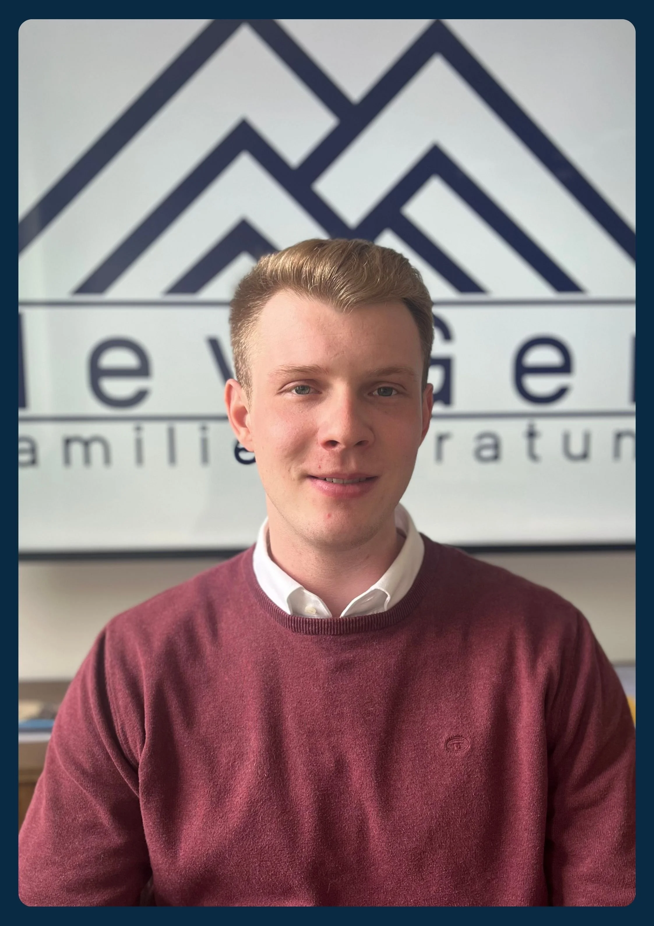 Junge Mann mit braunem Pullover und weißem Hemd vor firmeneigenem Hintergrund mit Logo, das Berge und den Schriftzug 'levege' zeigt.