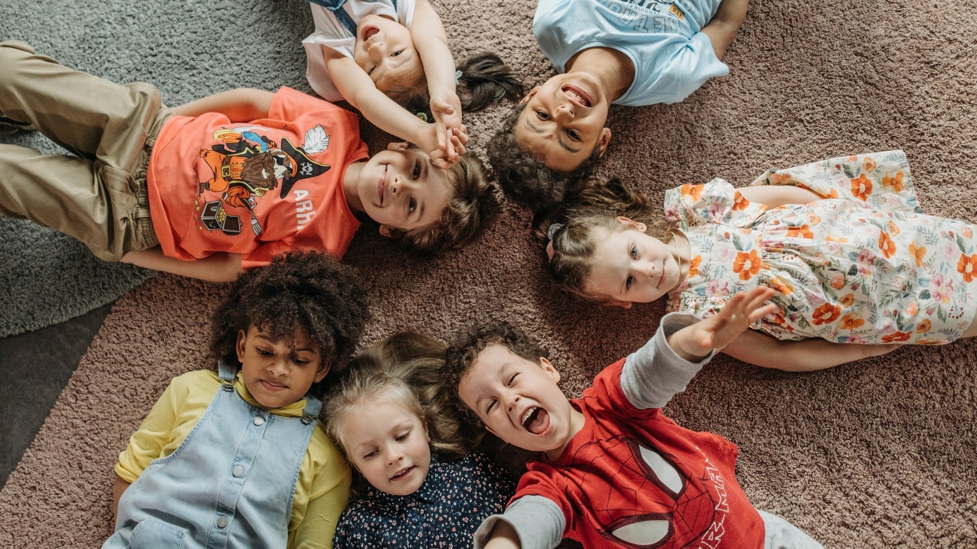 Mehrere Kinder liegen auf einem Teppich und schauen nach oben, lachen und machen Spaß.