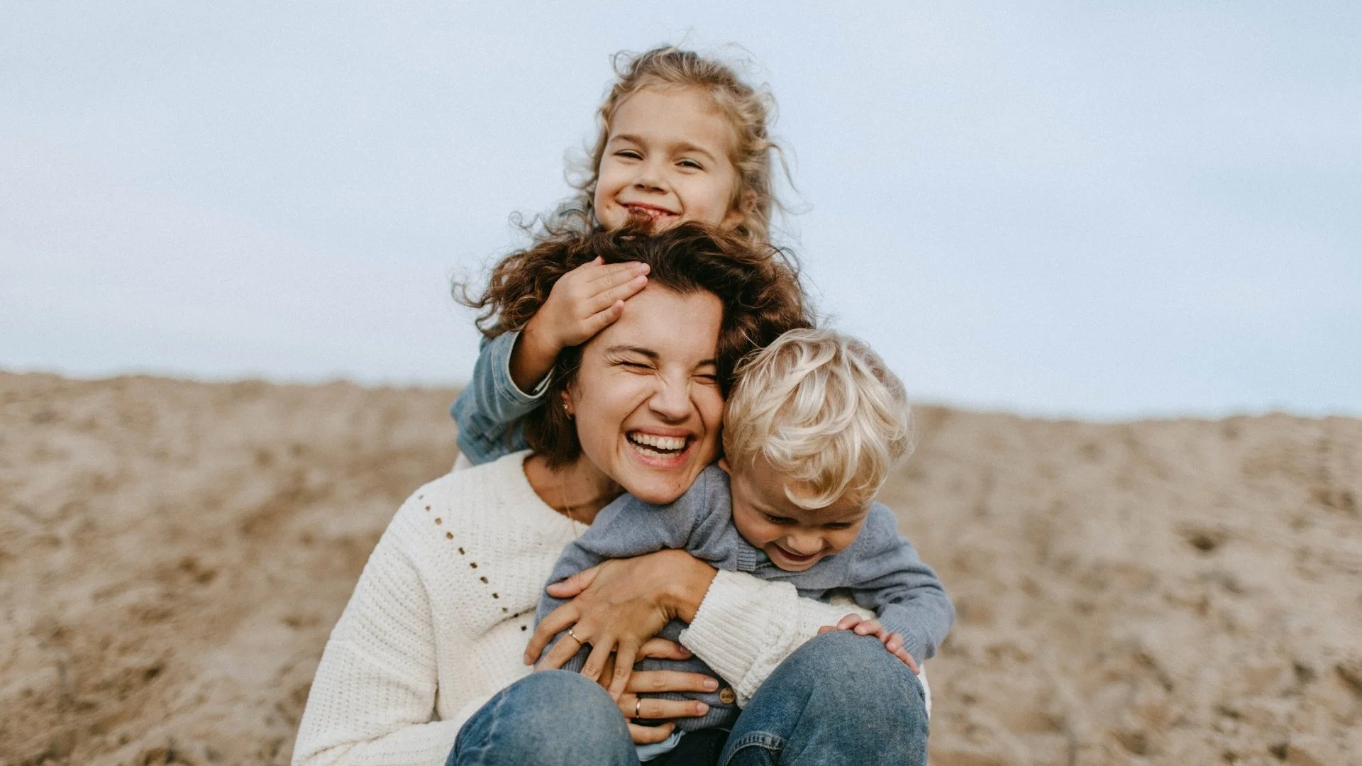 Lächelnde Frau mit zwei Kindern am Strand, die sich umarmen und Spaß haben.