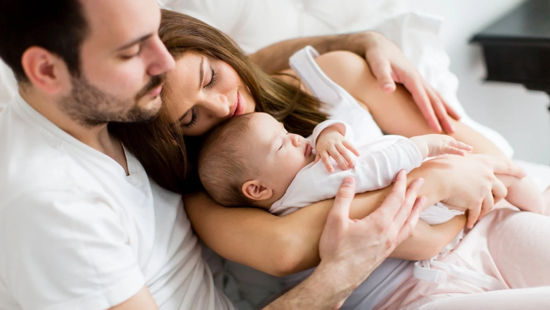 Familie beim Stillen eines Babys auf einem Bett in einer hellen, freundlichen Umgebung.