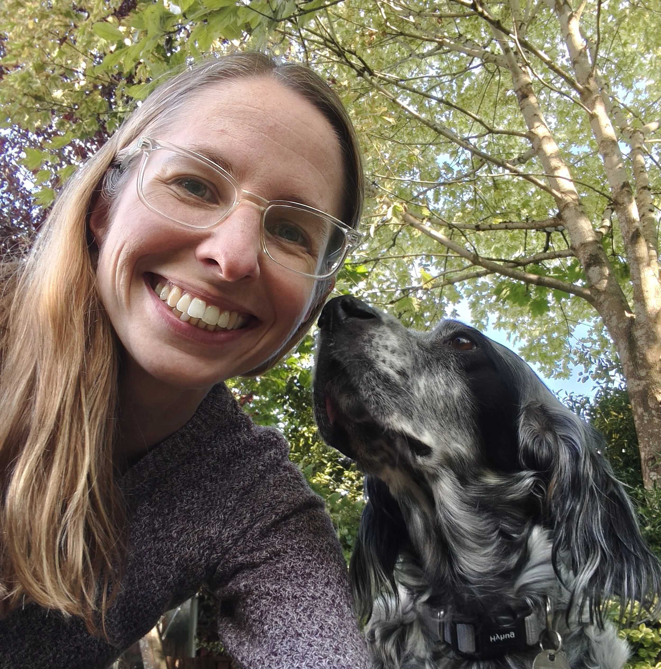 A lady with long hair under a tree with a black and white English Setter dog looking at her
