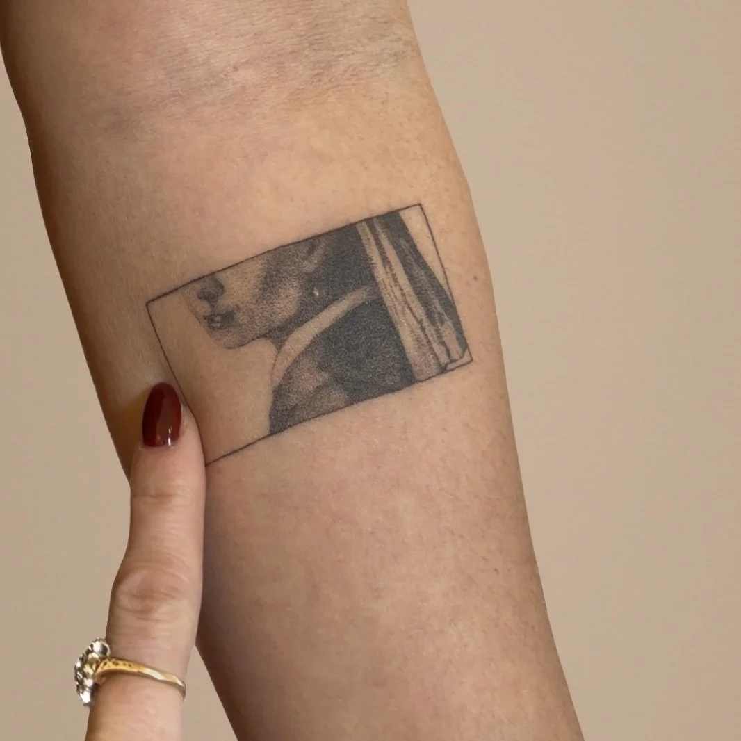 Tattoo of a dog wearing a sweater on a person's upper arm.