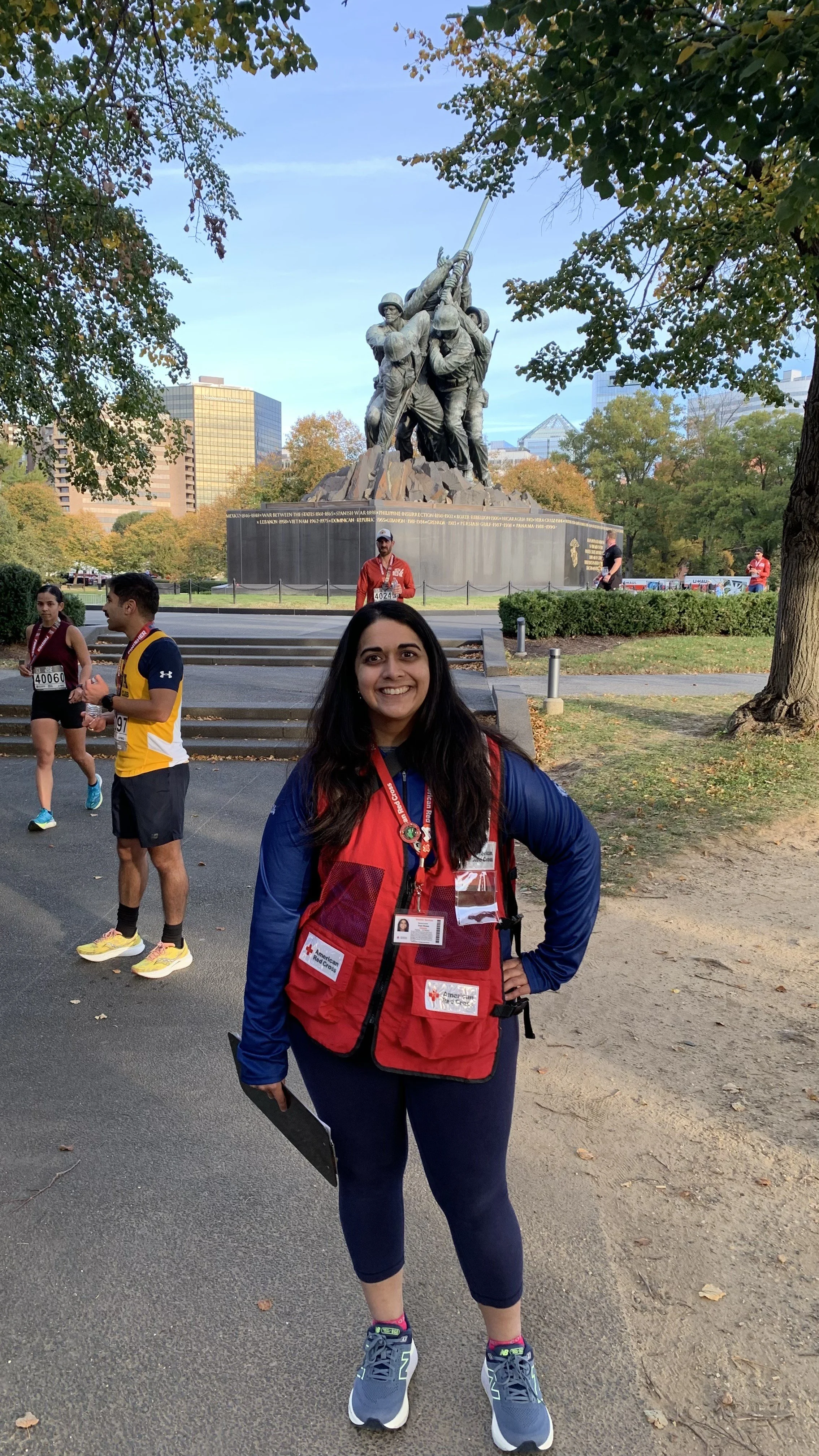 Person in red vest in front of Iwo Jima Memorial, with people running in background.