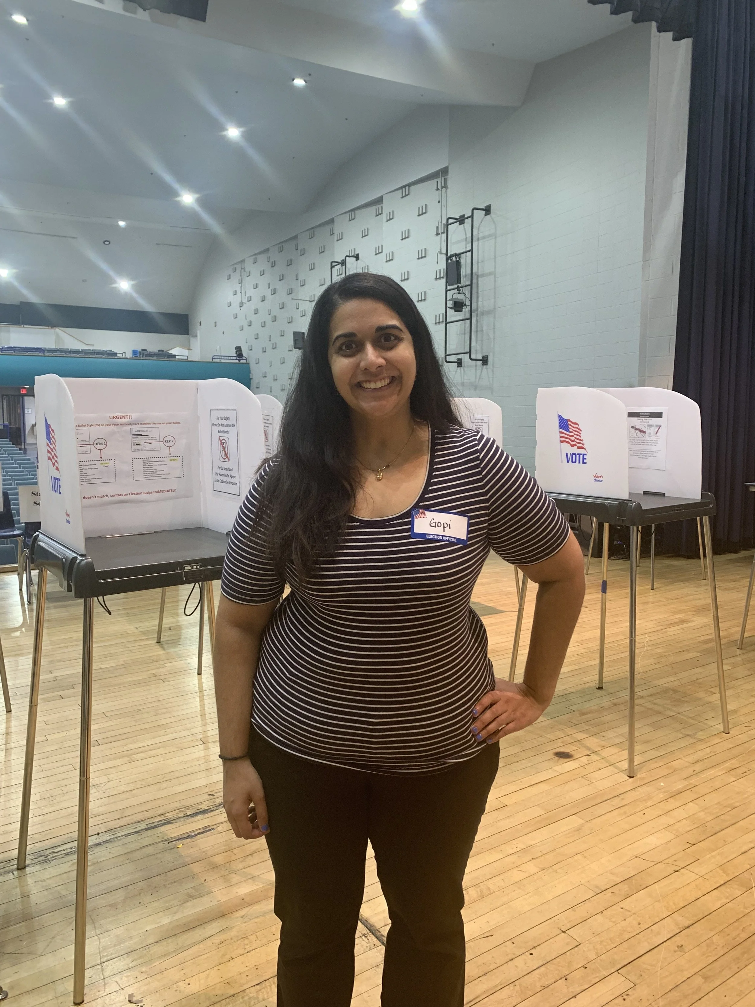 Candidate smiling while serving as election judge standing in a room with voting booths.