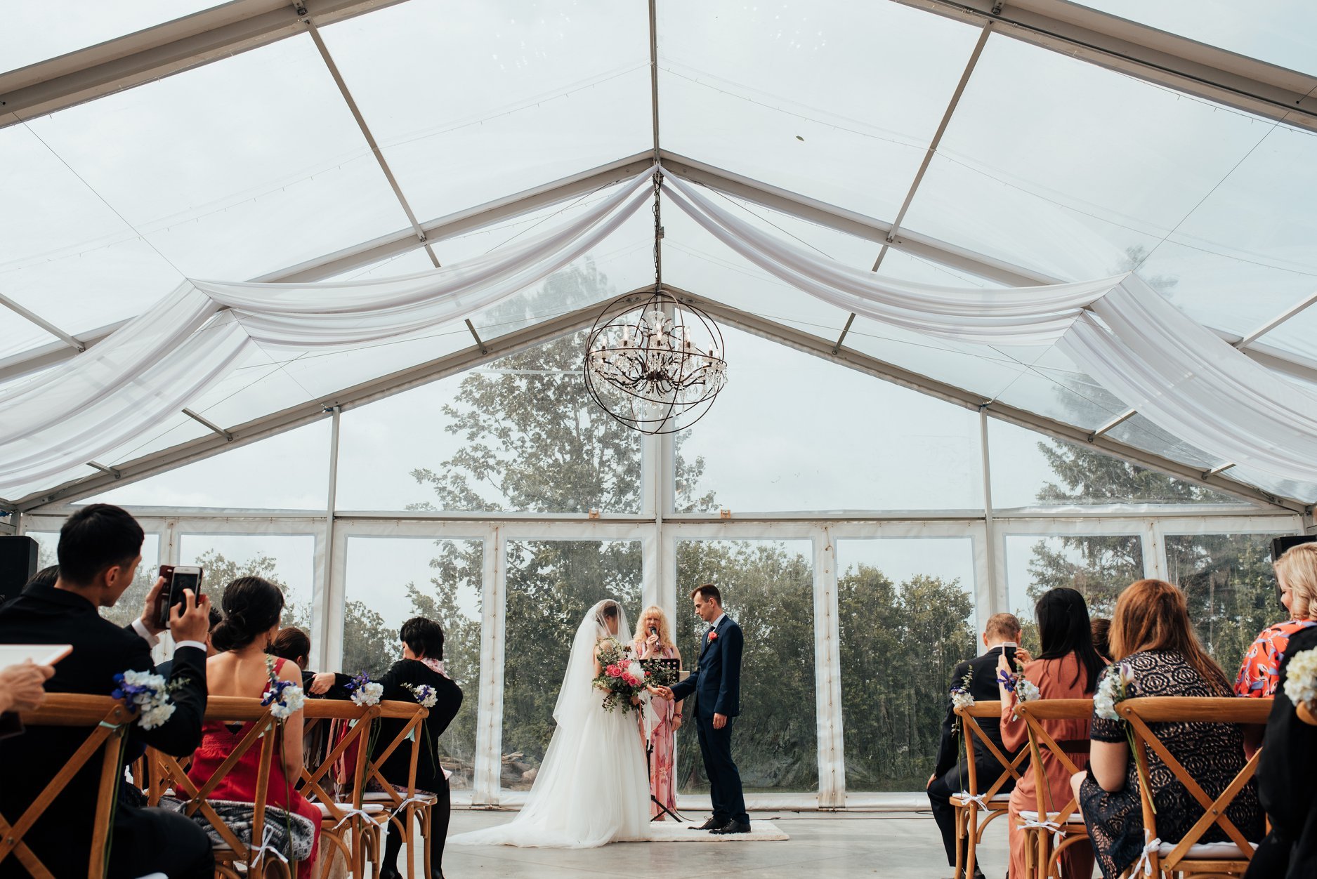 Bride and groom exchanging vows during a wedding ceremony inside Pine and Pond's clear tent venue in Alberta