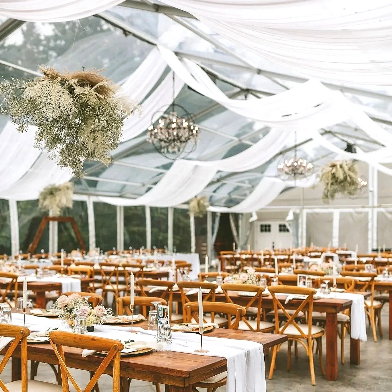Clear reception tent at Pine and Pond set for a wedding with wood tables, chandeliers, and greenery