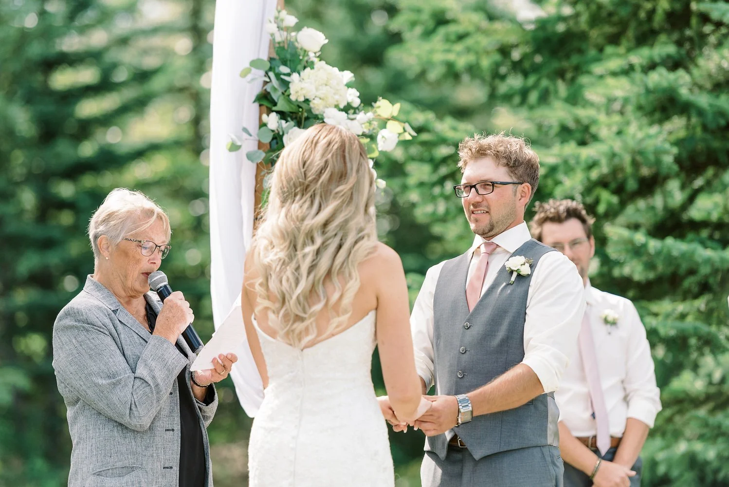 Bride and groom exchanging vows during an outdoor wedding ceremony at Pine and Pond surrounded by trees in Alberta