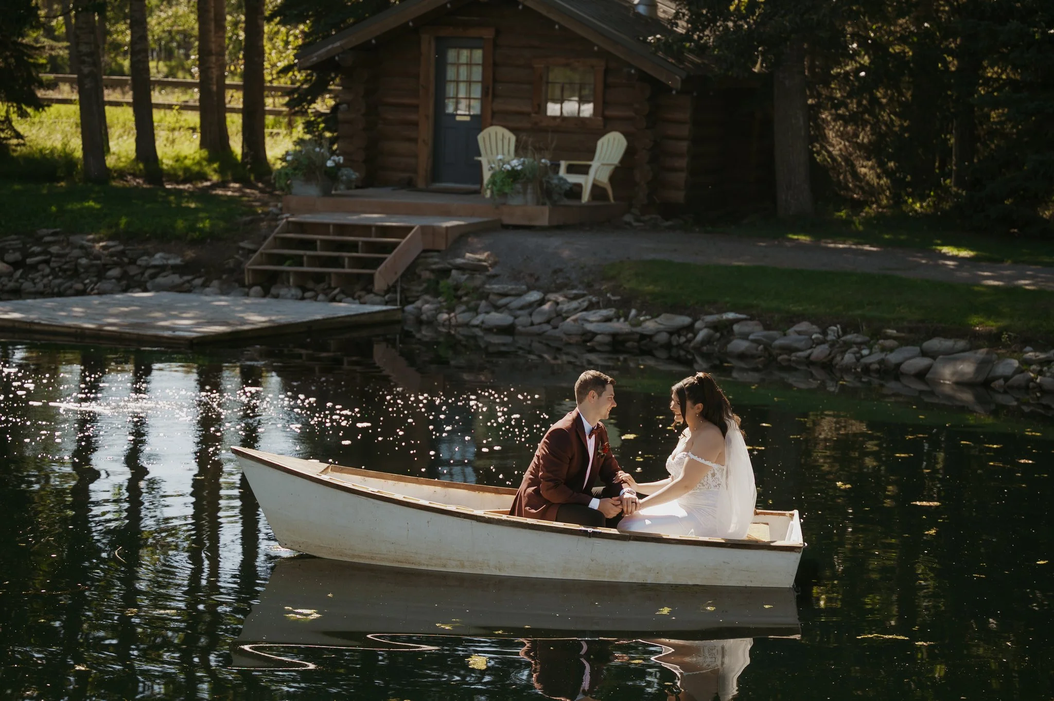 A bride and groom share a romantic moment in a rowboat on Pine and Pond's pond, with the honeymoon cabin creating one of Alberta's most memorable wedding backdrops.