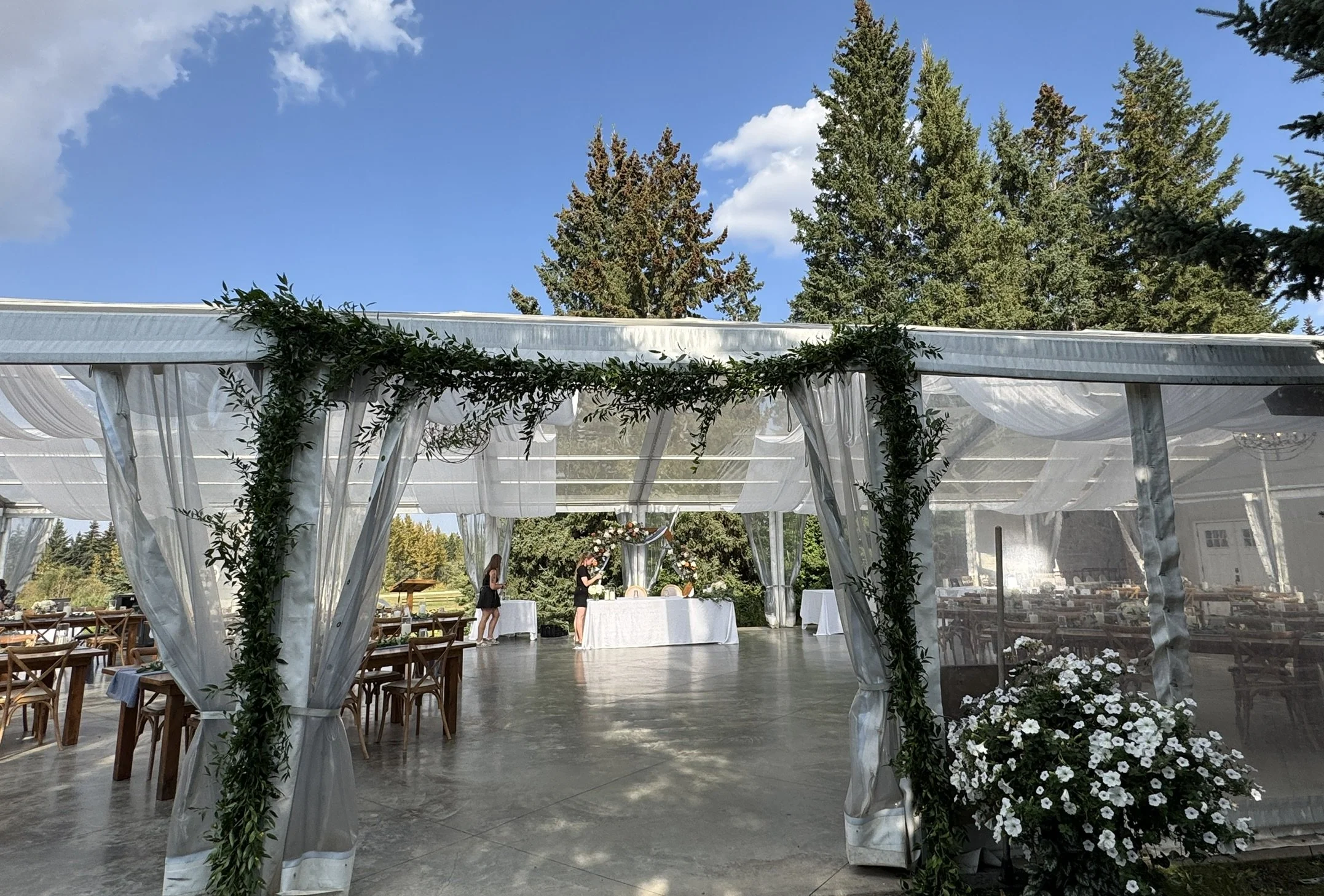 Clear tent wedding reception space at Pine and Pond Wedding Venue, styled with greenery, draping, and wooden tables for an elegant outdoor celebration in Central Alberta.