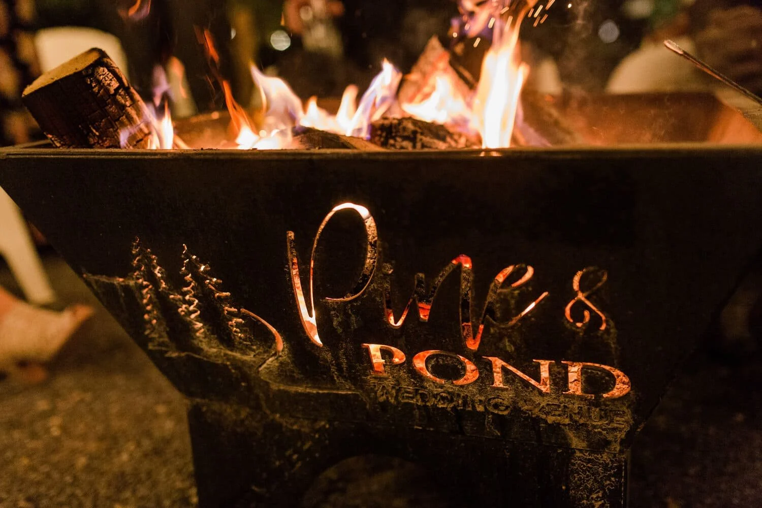 Outdoor fire pit glowing during an evening wedding reception at Pine and Pond