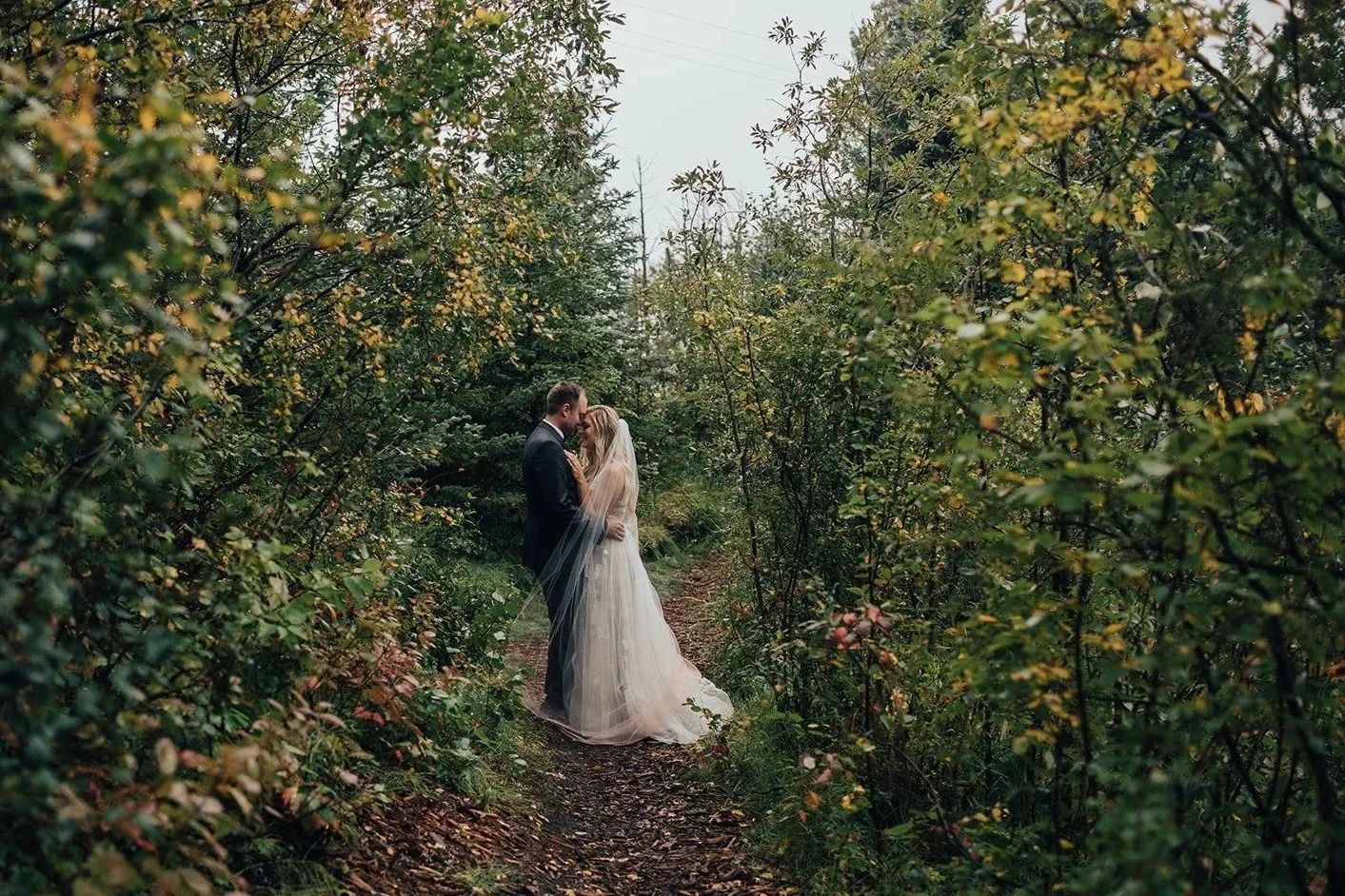 Bride and groom embracing on a forest path at Pine and Pond Wedding Venue