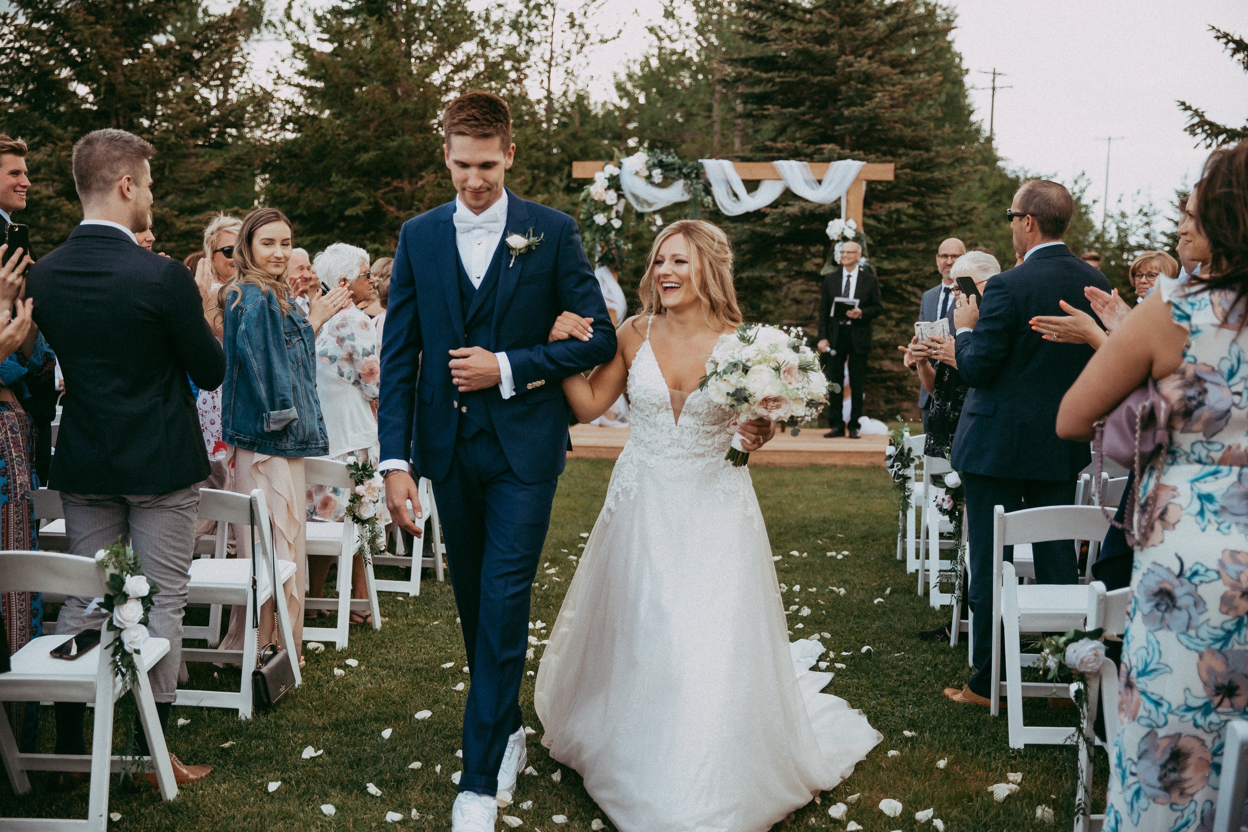 A newly married couple celebrates their outdoor wedding ceremony at Pine and Pond, surrounded by family, friends, and the natural beauty of Central Alberta.
