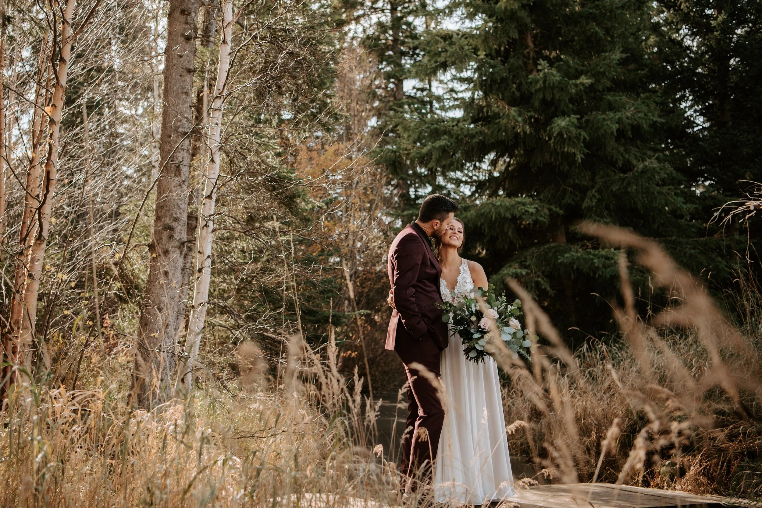 Bride and groom sharing a romantic moment on a forest trail at Pine and Pond outdoor wedding venue in Alberta