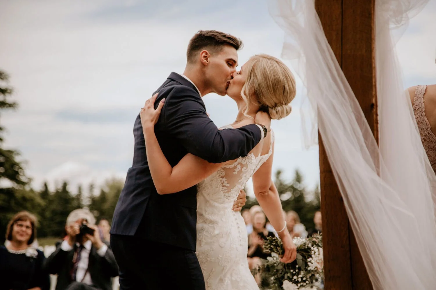 Bride and groom sharing their first kiss during an outdoor wedding ceremony at Pine and Pond