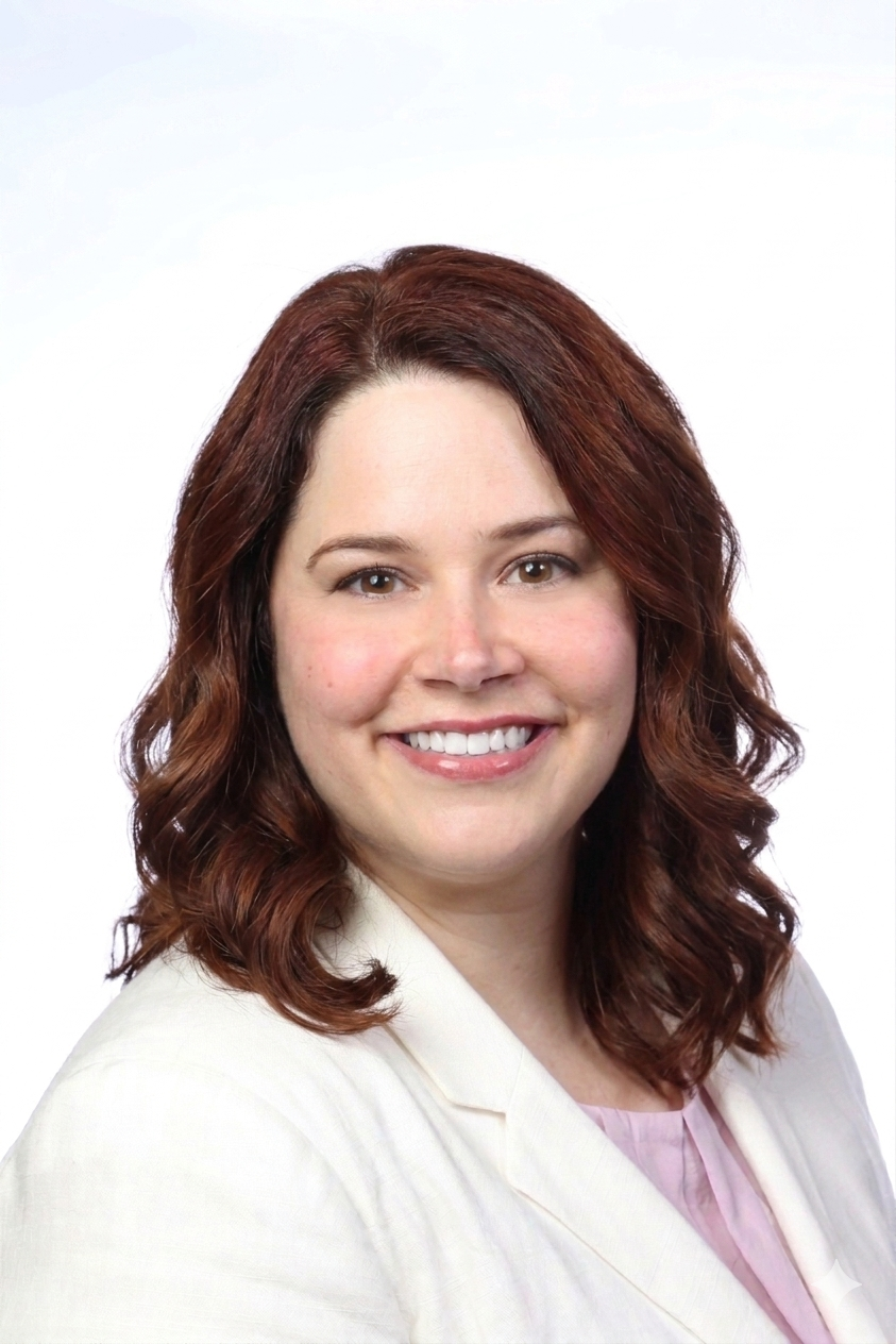 Portrait of a woman with shoulder-length brown curly hair, smiling, wearing a light-colored blazer and pink top, against a white background.