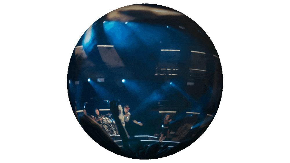 Reflective spherical surface showing a stage with performers, stage lights, and audience in a concert or event setting.