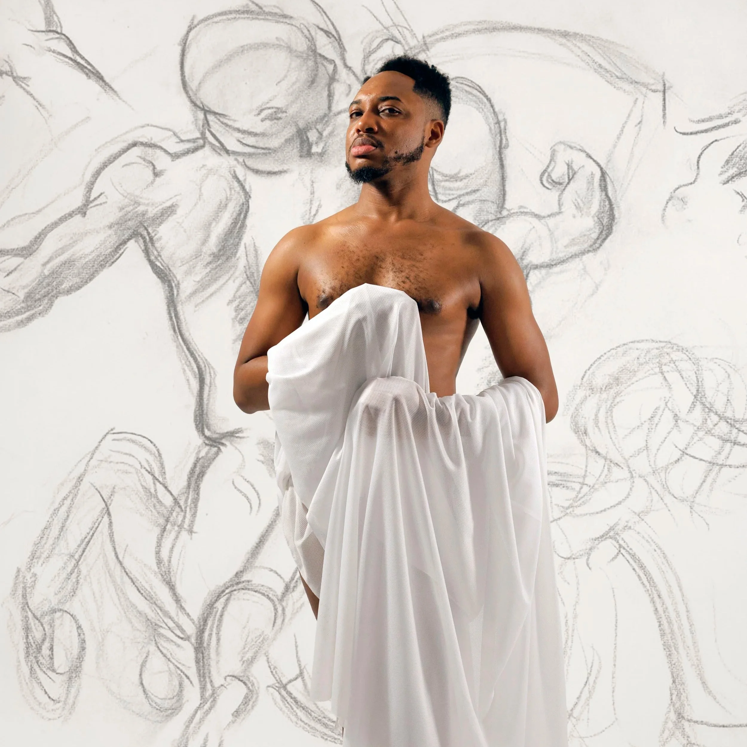 Photo of a shirtless man with short hair and a beard standing in front of a wall with an art sketch of a muscular figure in a similar pose.