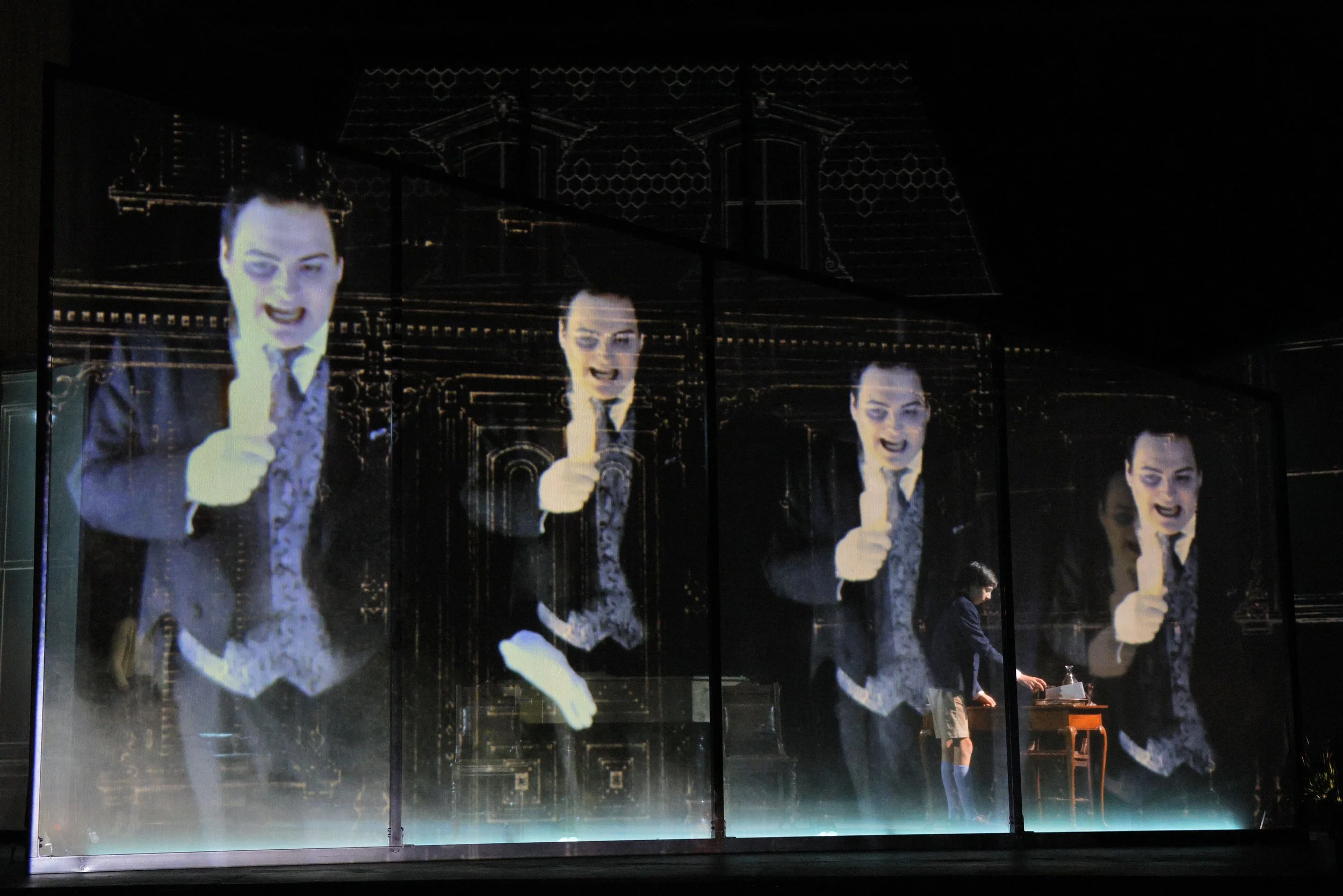 A display featuring multiple large, mirrored projections of a man in a suit, holding a microphone, with a dark, ornate background.